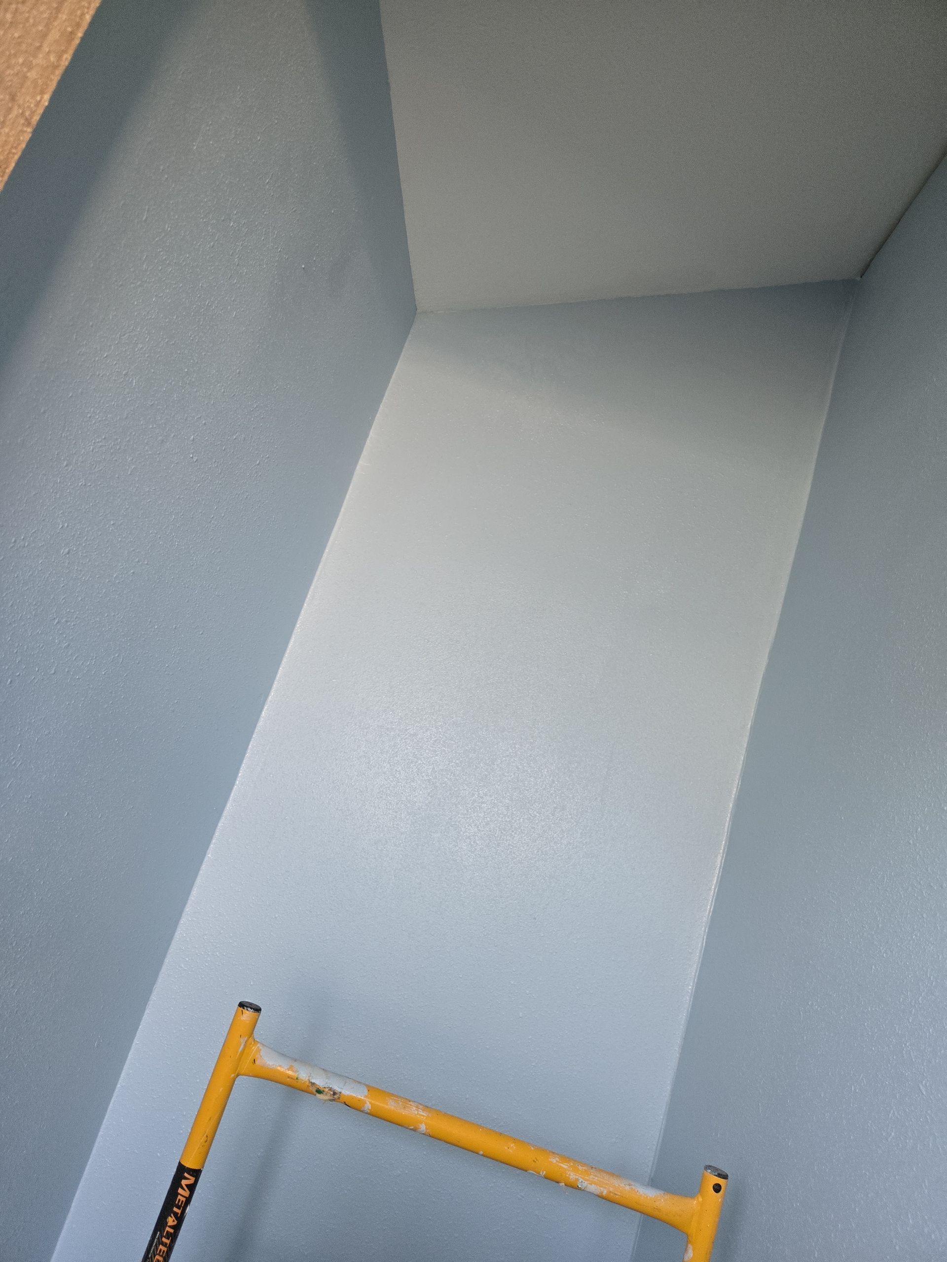 Interior corner of a light gray room with a yellow step ladder below.