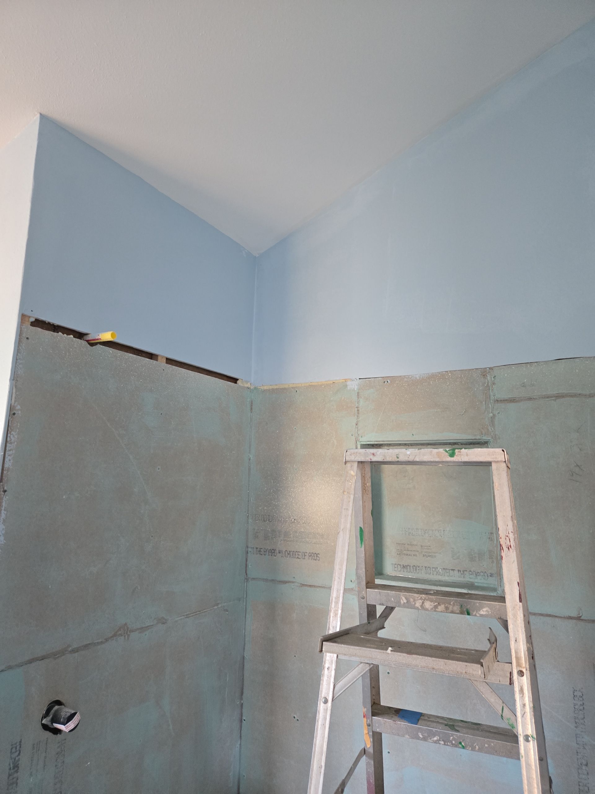 Bathroom shower area under renovation with pale blue walls and a step ladder.