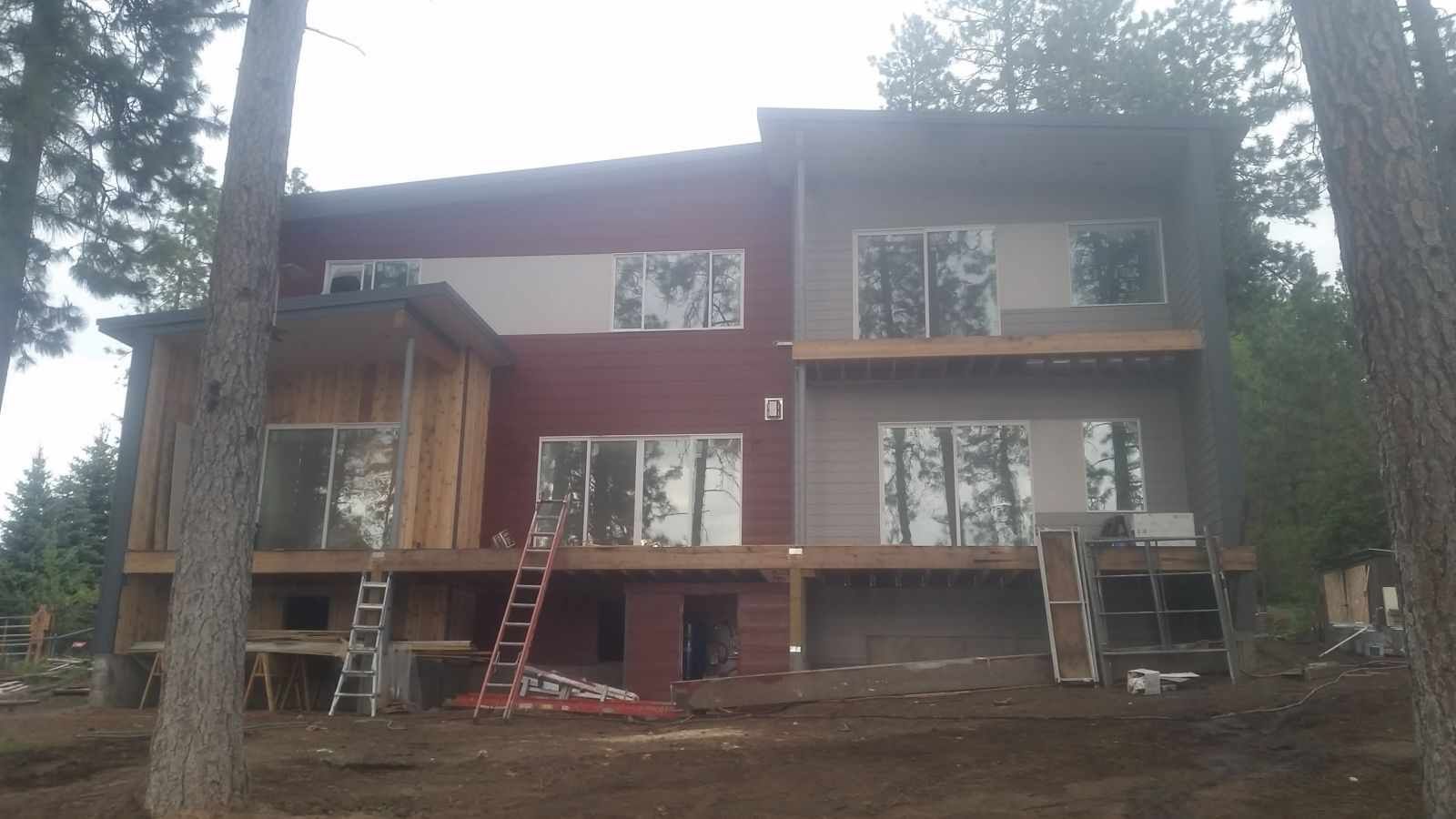 Partially built two-story house with red siding and large windows in a wooded area