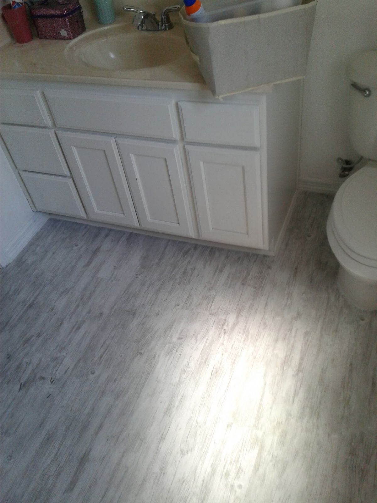 Bathroom with white vanity and toilet beside a light gray wood-look floor.