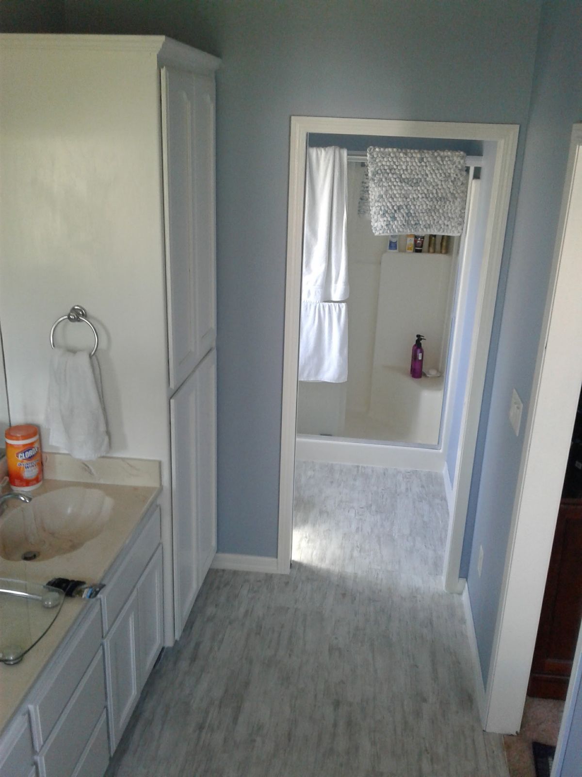 Narrow bathroom with white cabinets, sink, and blue walls leading to a doorway into another room.