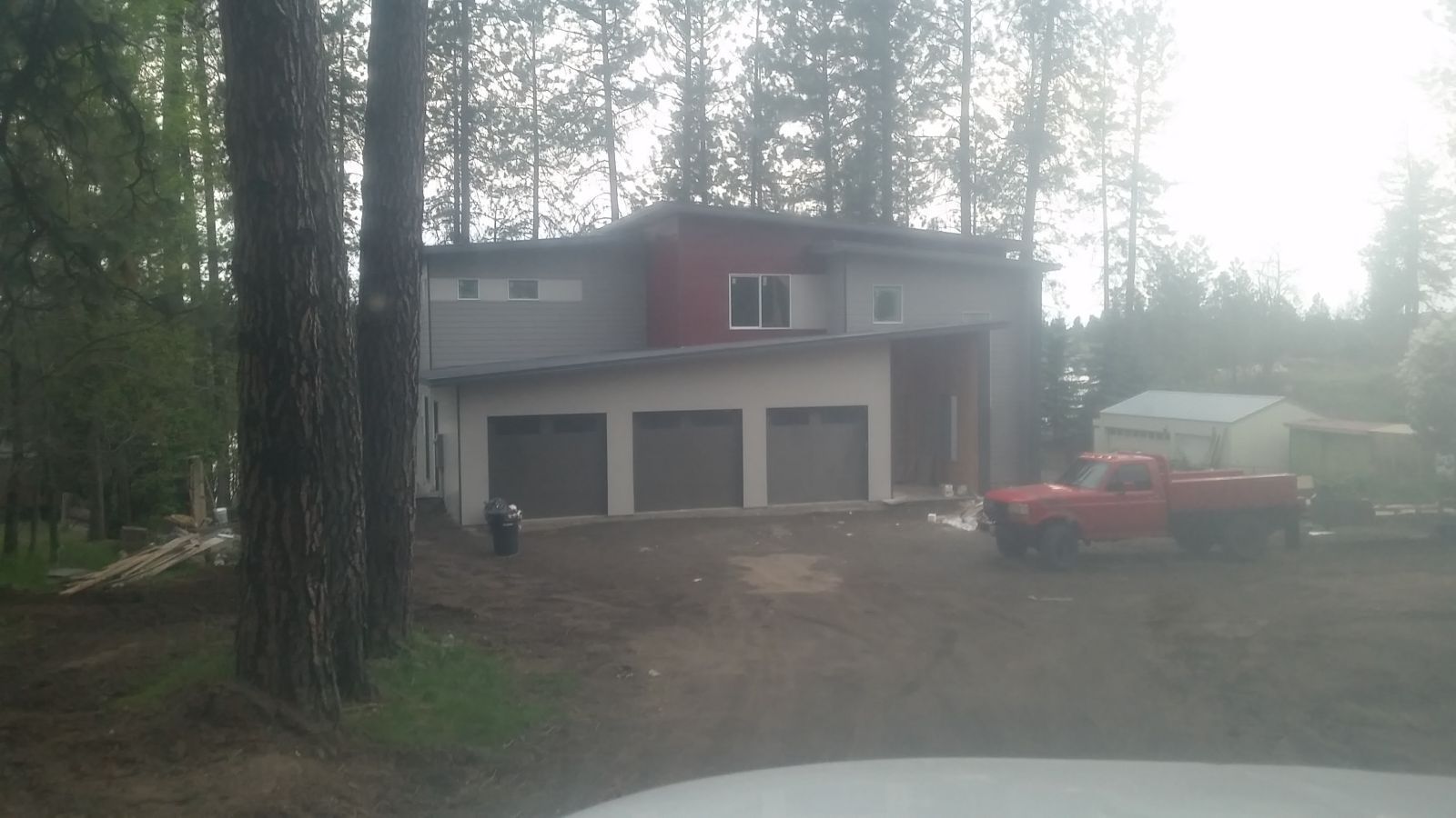 Two-story house in a wooded lot with a red truck parked outside and garage doors visible
