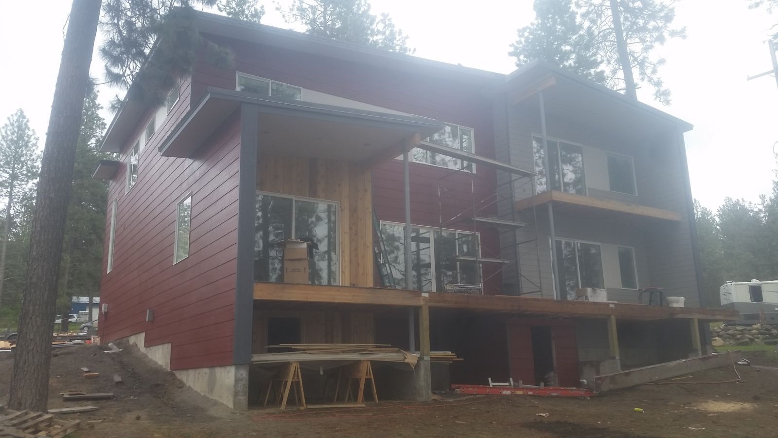 Red two-story house under construction with a covered porch and trees around it
