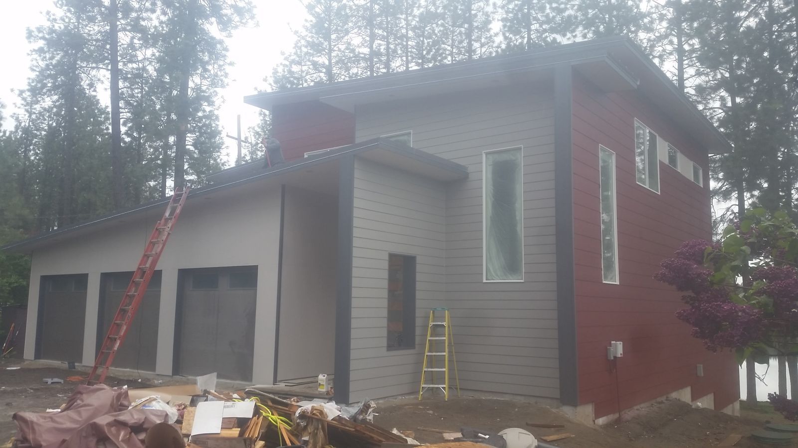 House exterior under construction with gray siding, red trim, ladder, and piles of debris in front