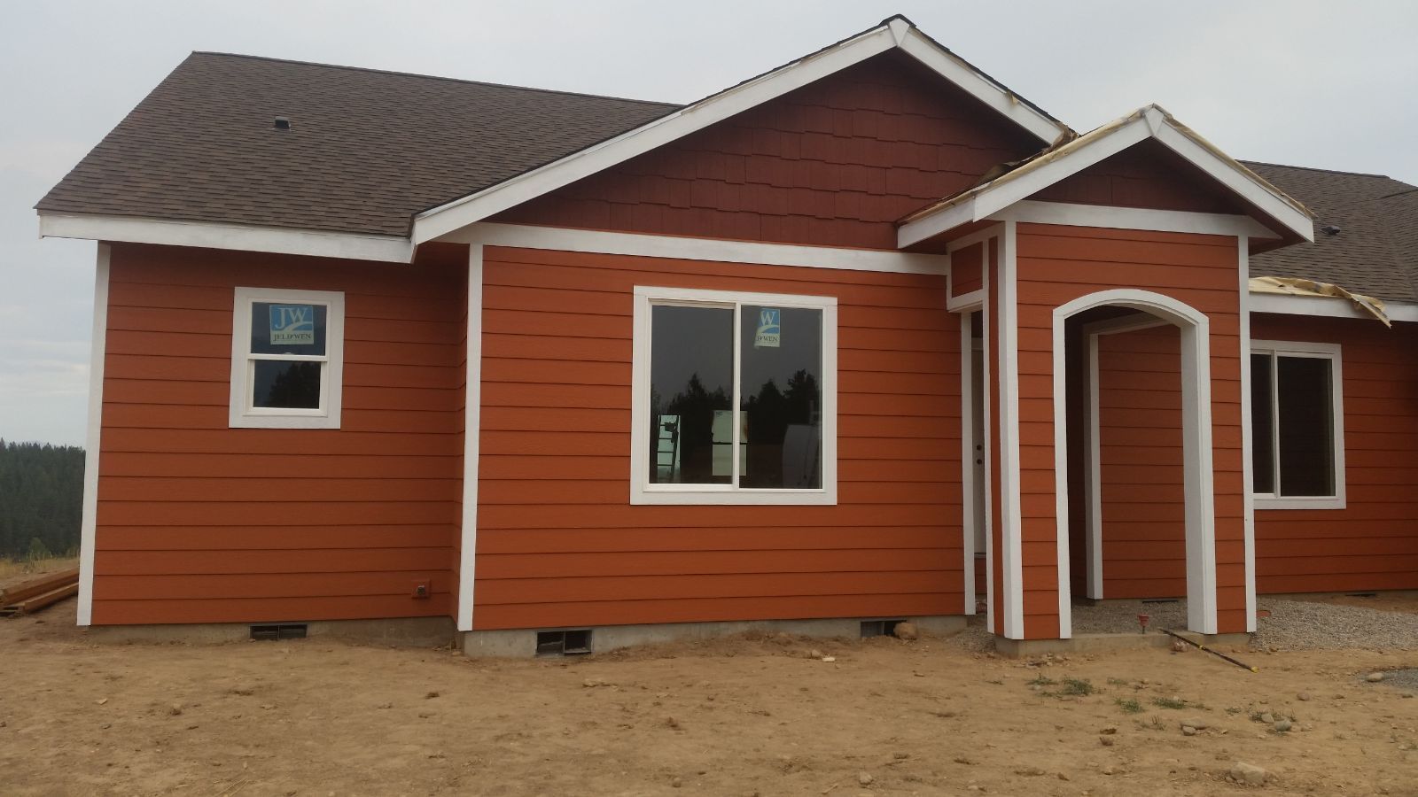 Small red house with white trim and a covered front entrance on a dirt lot.