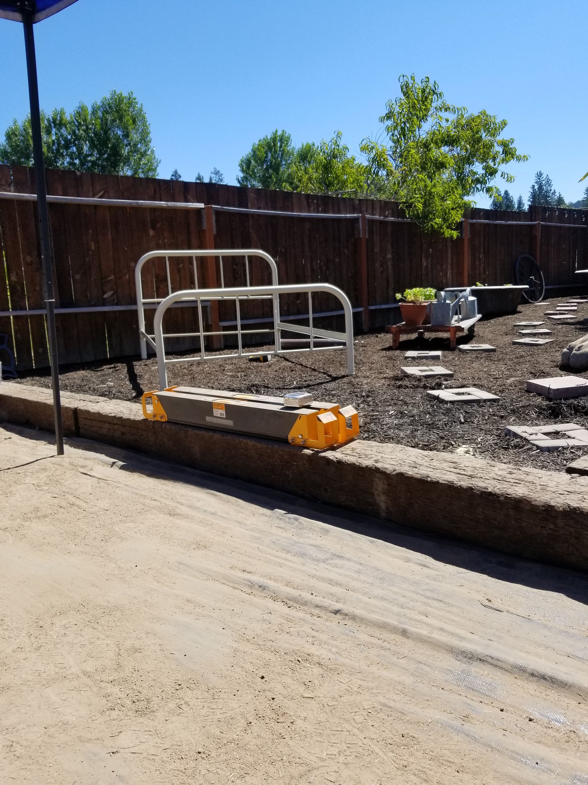 Outdoor construction area with white metal railings, gravel, and stepping stones beside a fence.