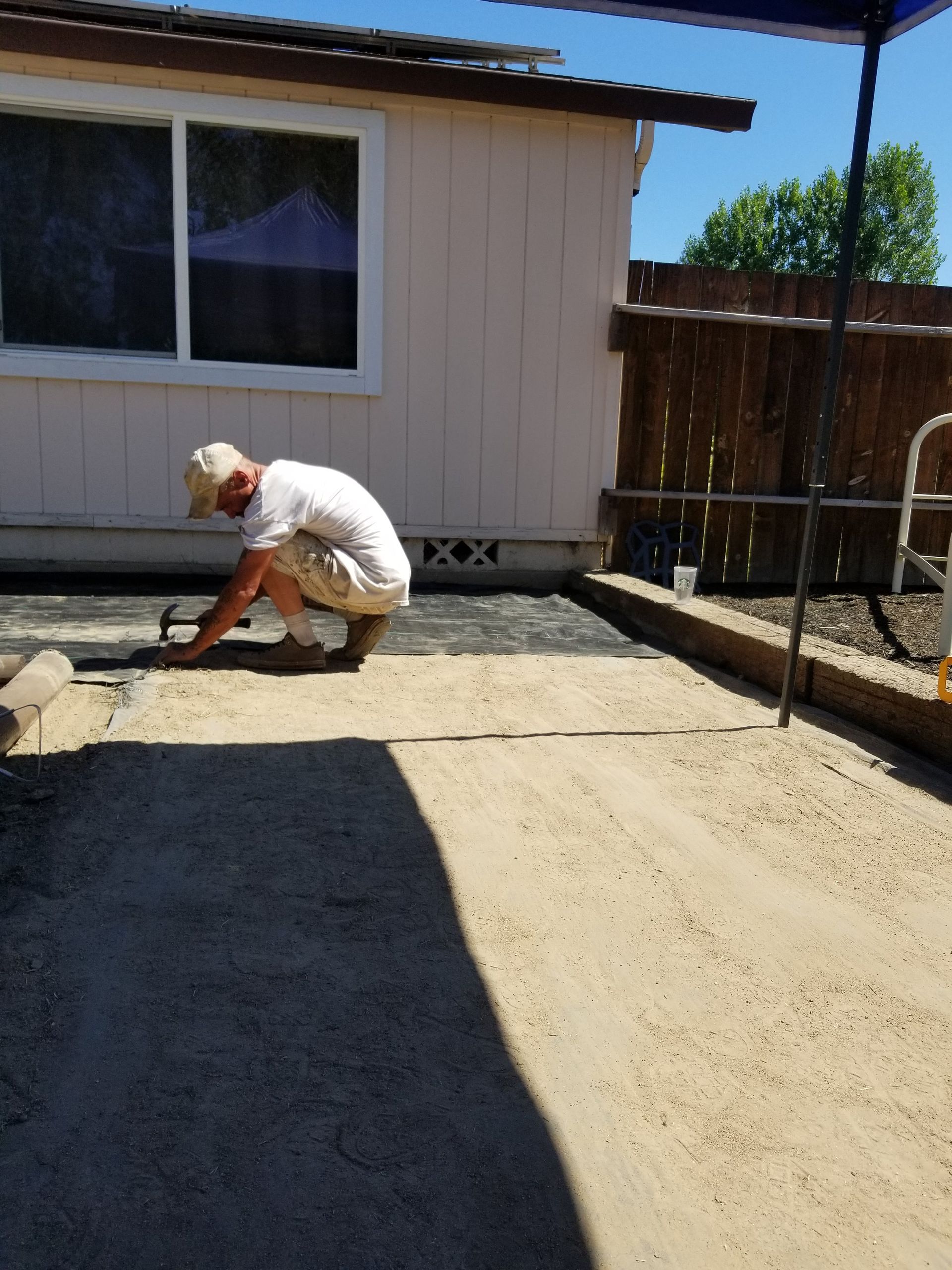 Worker smoothing a concrete patio beside a beige house in bright sunlight.