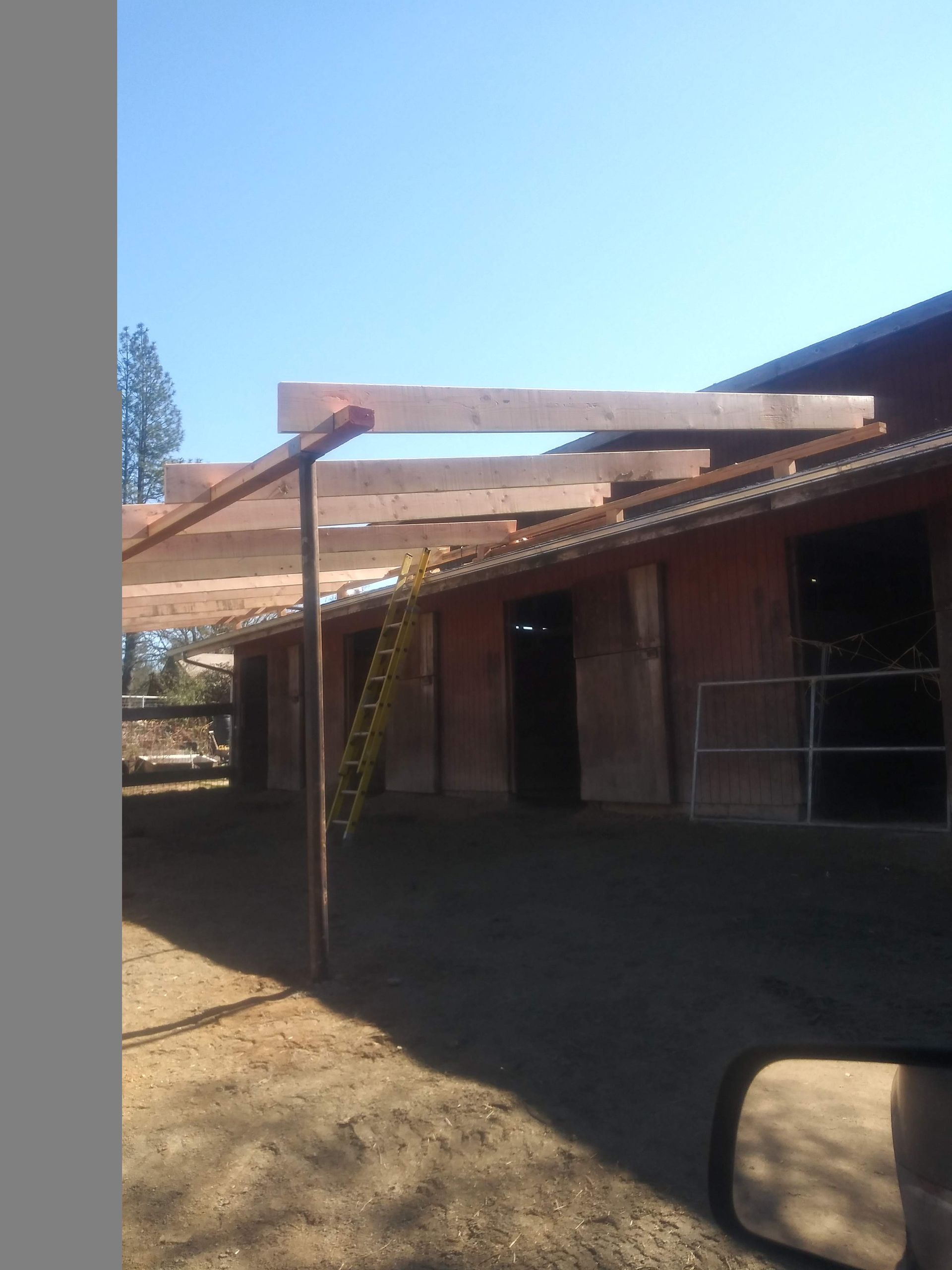 Partly built porch with wooden beams and red brick building under a clear blue sky