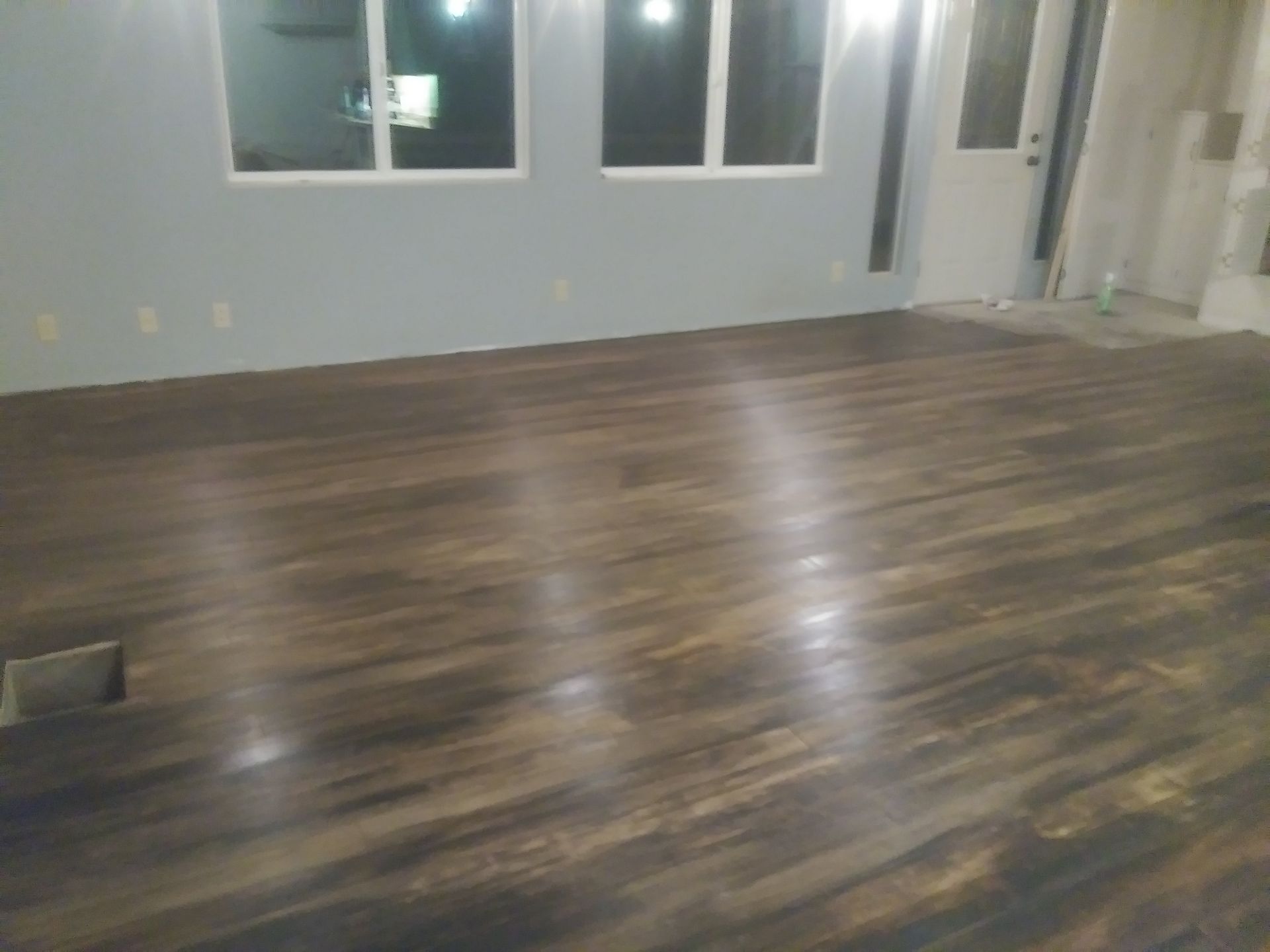 Empty room with wood-look flooring, gray walls, and windows reflecting light from outside