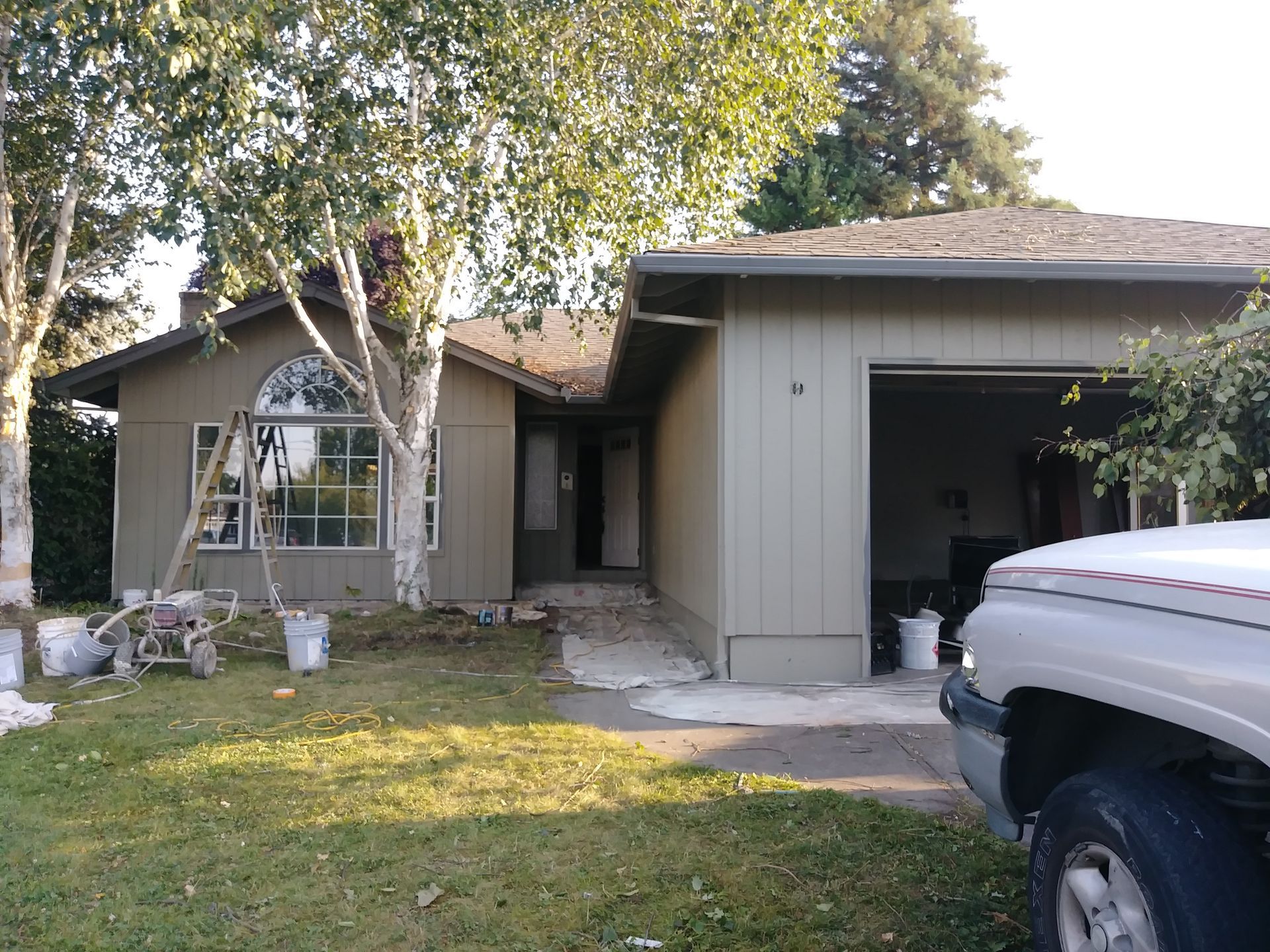 Single-story house with a garage, front window, and driveway under trees, with a truck in the foreground