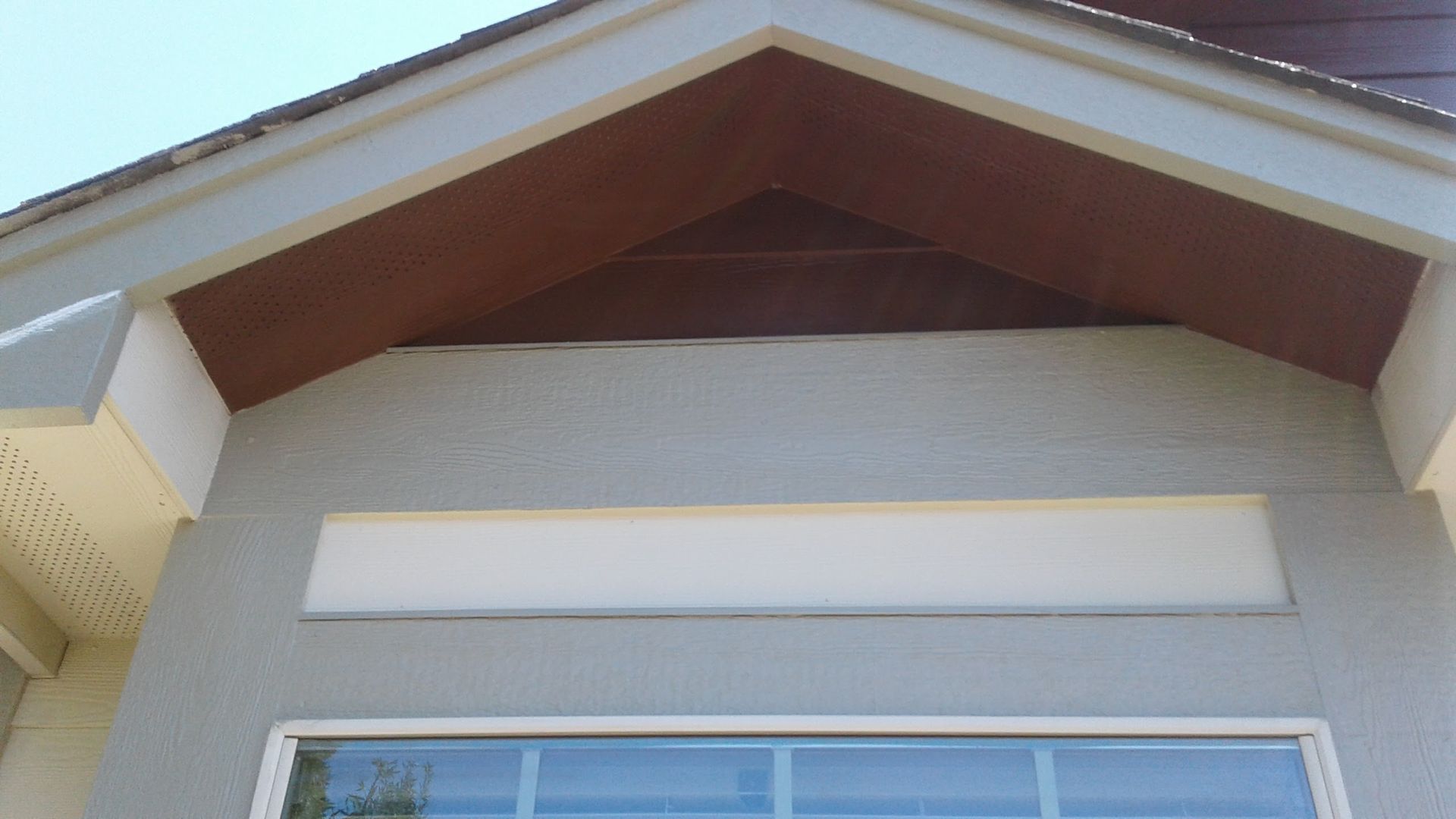 Exterior of a house roof with beige siding, white trim, and a dark wood gable