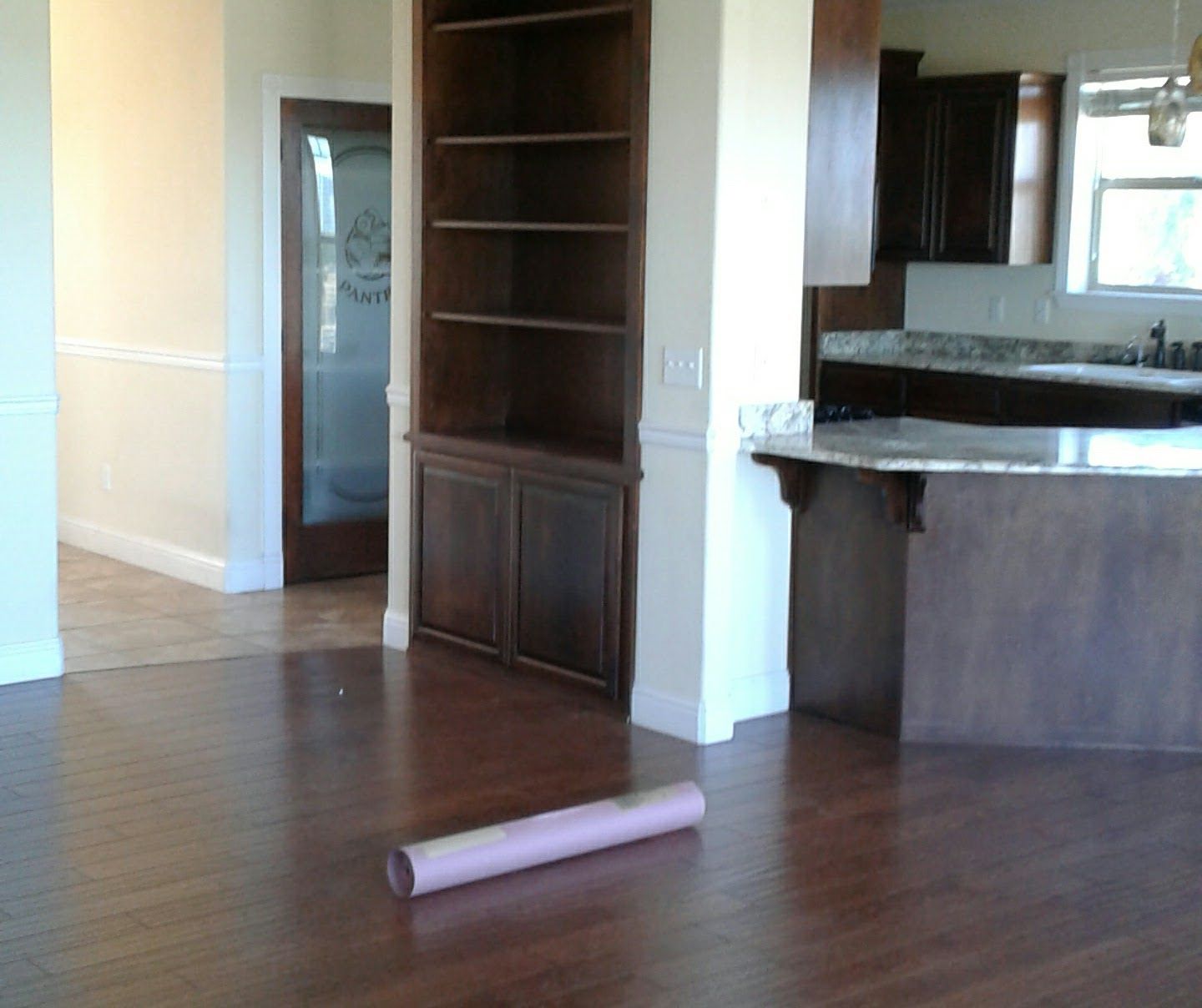 Empty room with hardwood floor, built-in shelves, and a pink rolled mat on the floor