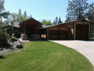 Log cabin-style house with garage, curved driveway, and green lawn in a wooded setting