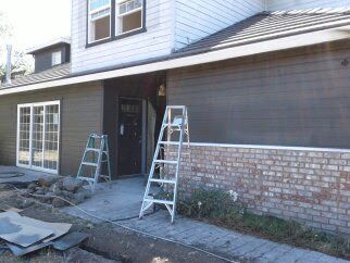 House exterior with ladders, exposed siding, and construction debris by the front entrance