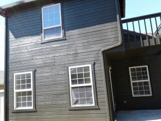 Dark gray house exterior with white-trimmed windows and an upper deck.