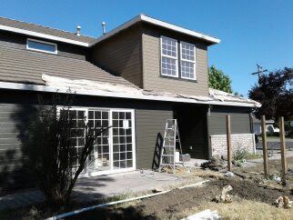 Two-story house exterior with patio, ladder, and construction debris in the yard