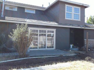 Two-story house exterior with gray siding, large windows, and a small front patio.