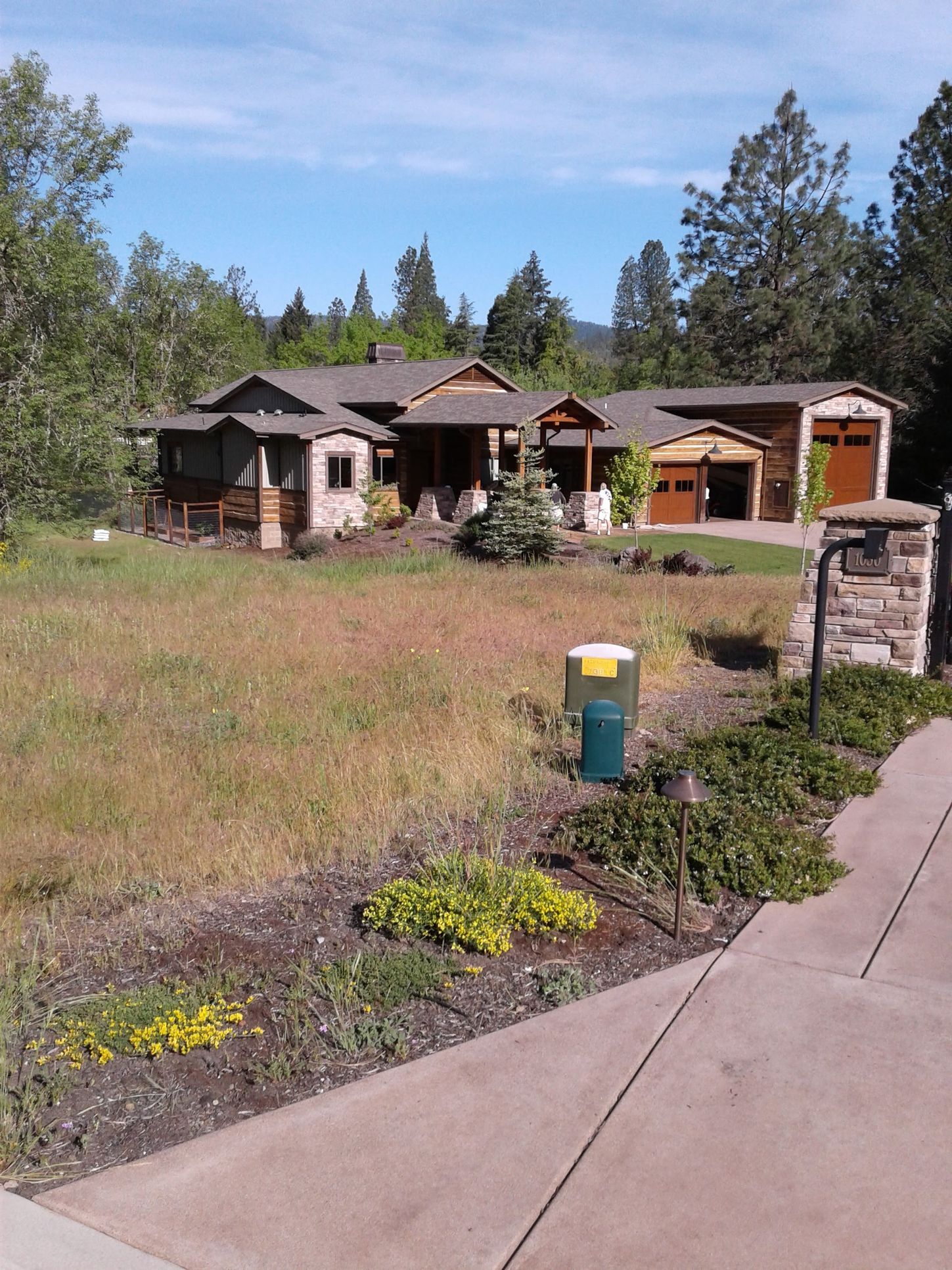 Rustic house with garage in a grassy yard under a blue sky, viewed from a concrete path.