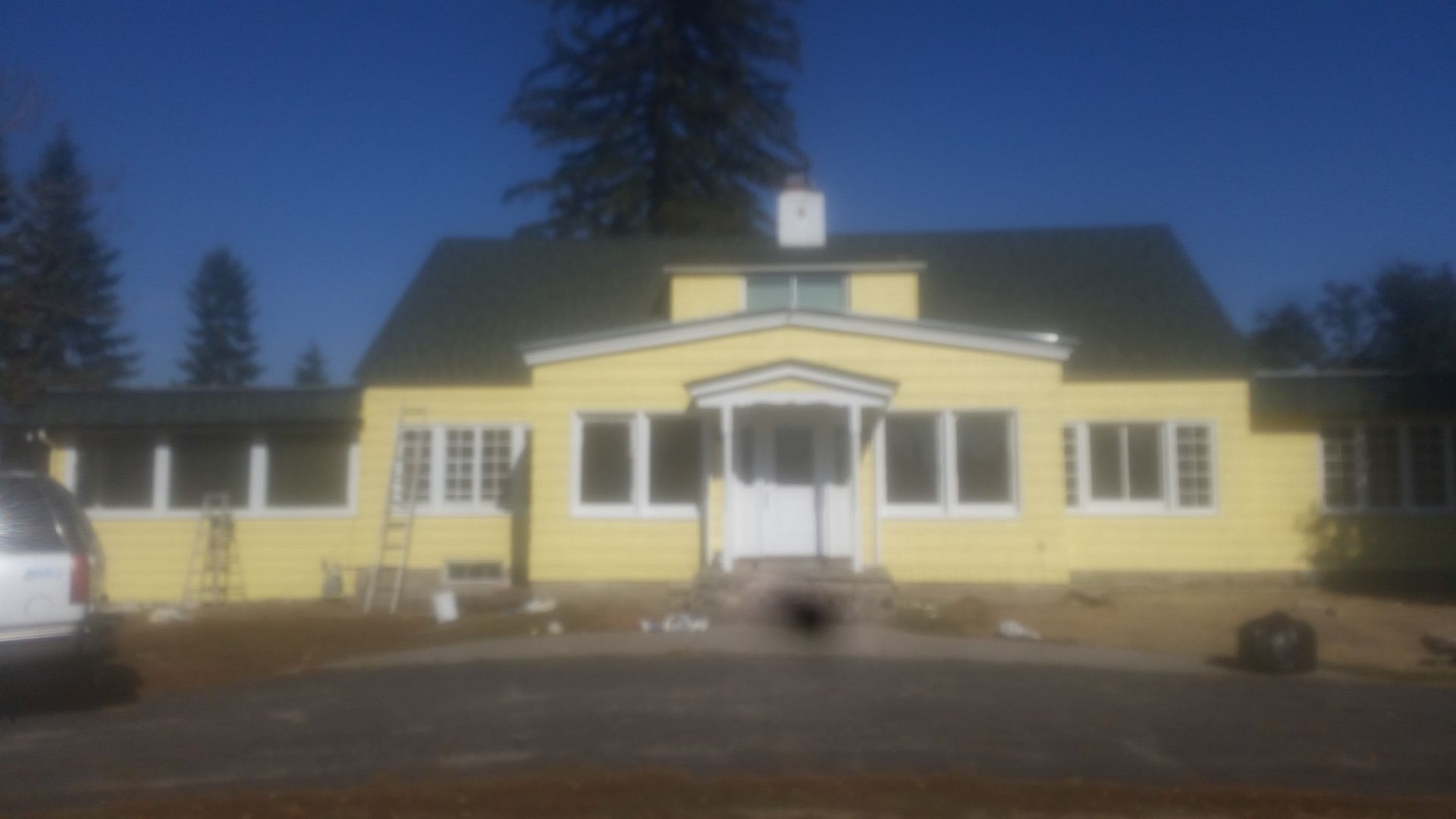 Yellow building with white trim and a central entrance under a dark roof at dusk