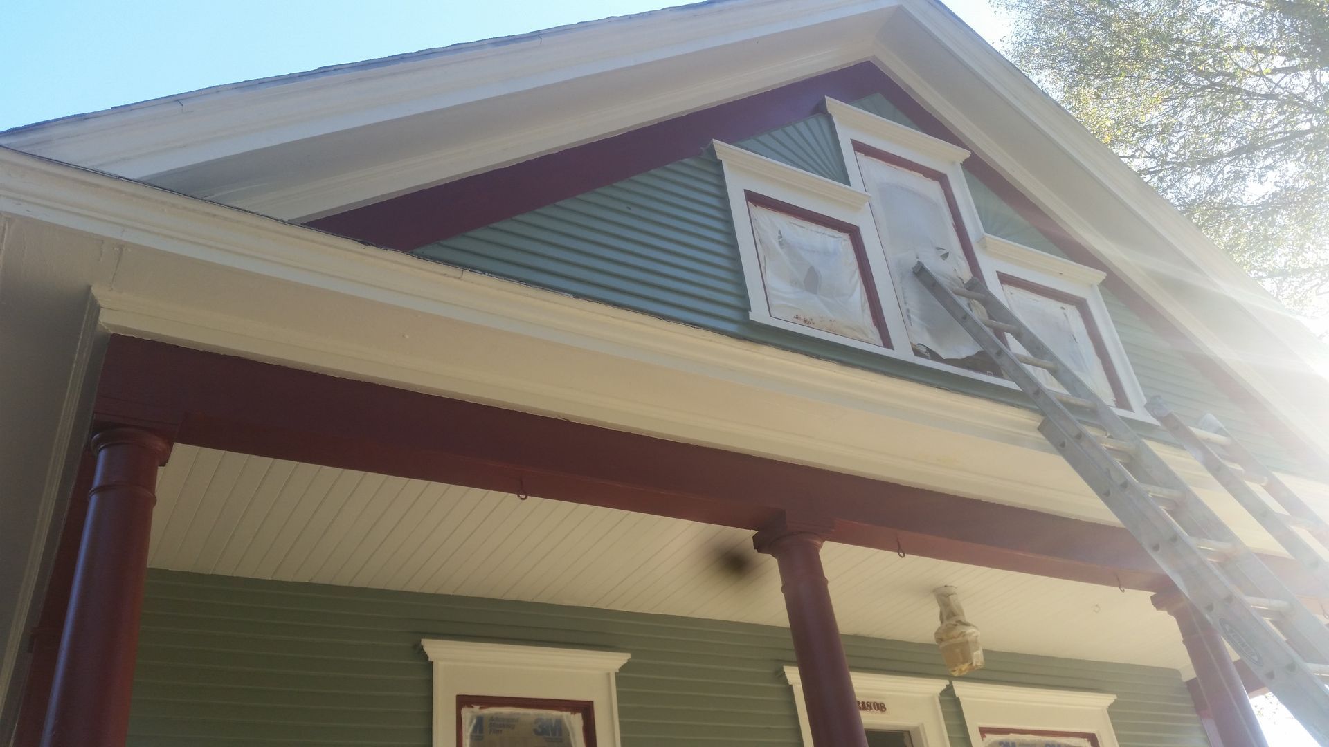 Two-story house exterior with green siding, maroon trim, and a ladder leaning against the roof.