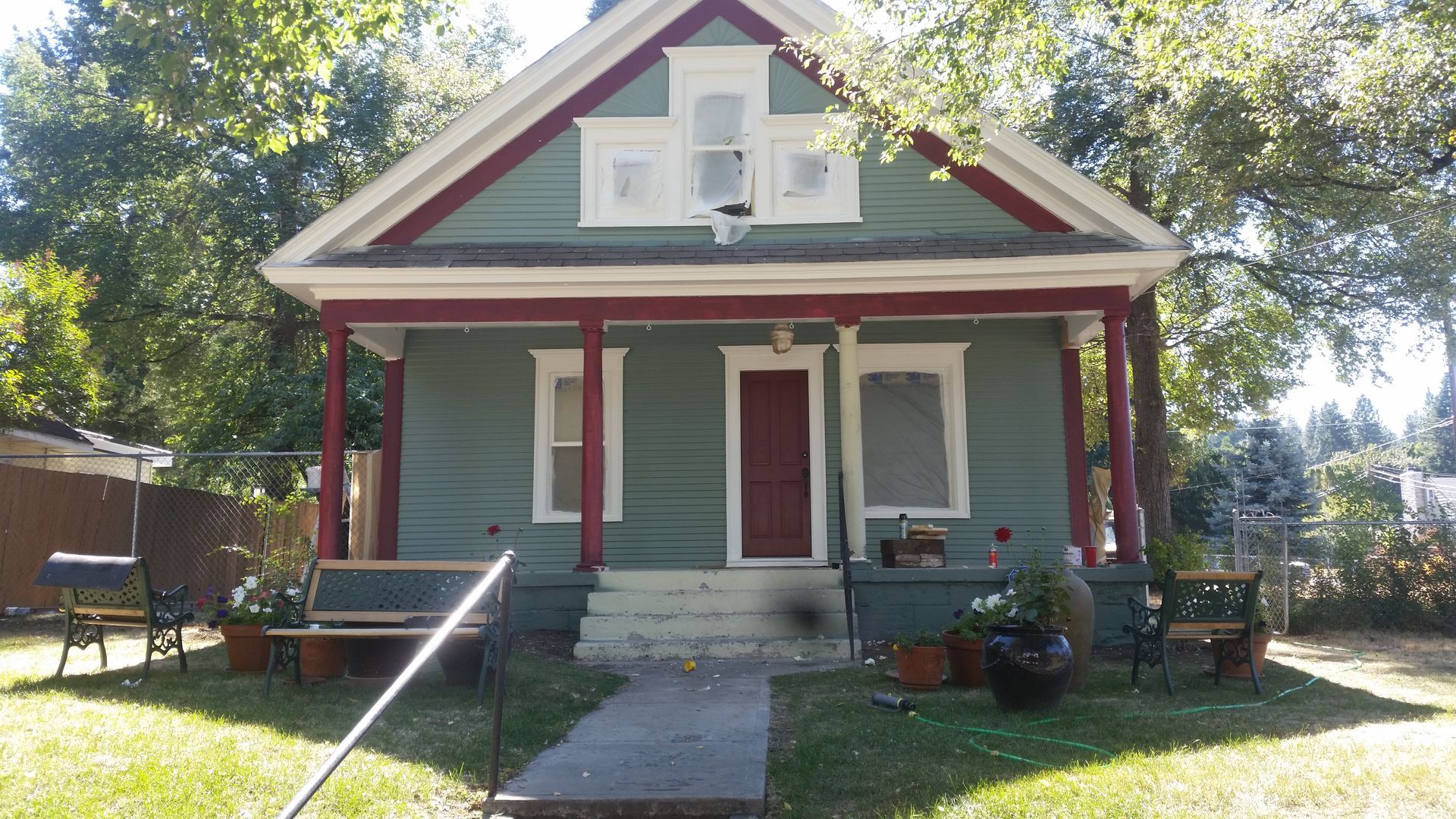 Small gray house with red trim, front porch, and a walkway in a sunny yard.