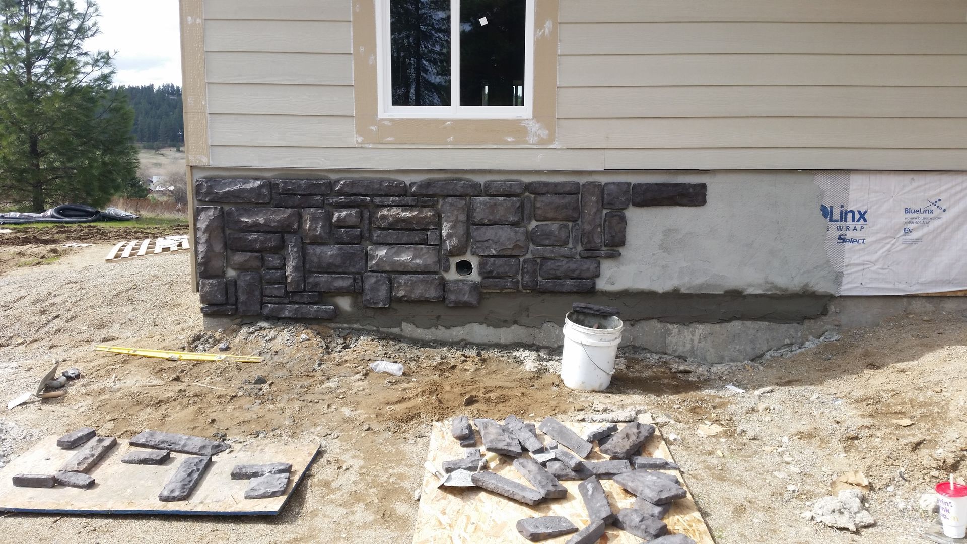 House exterior with partially finished stone veneer and construction materials on the ground