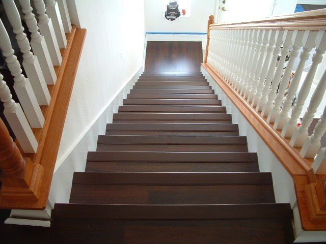 Indoor wooden staircase with white railings and brown steps, viewed from the top looking down.