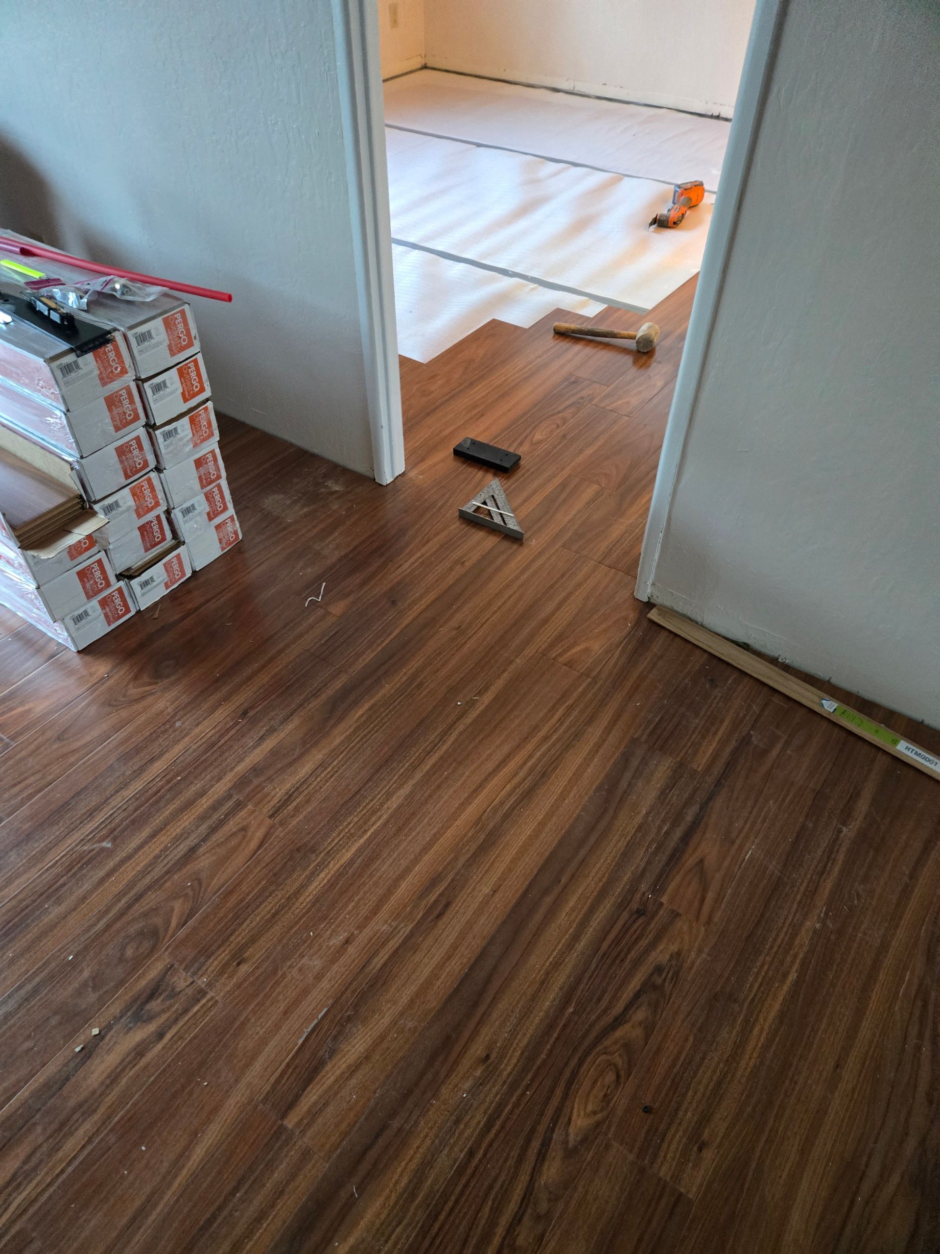Hallway with wood flooring leading to a white room; tools and debris scattered on the floor.