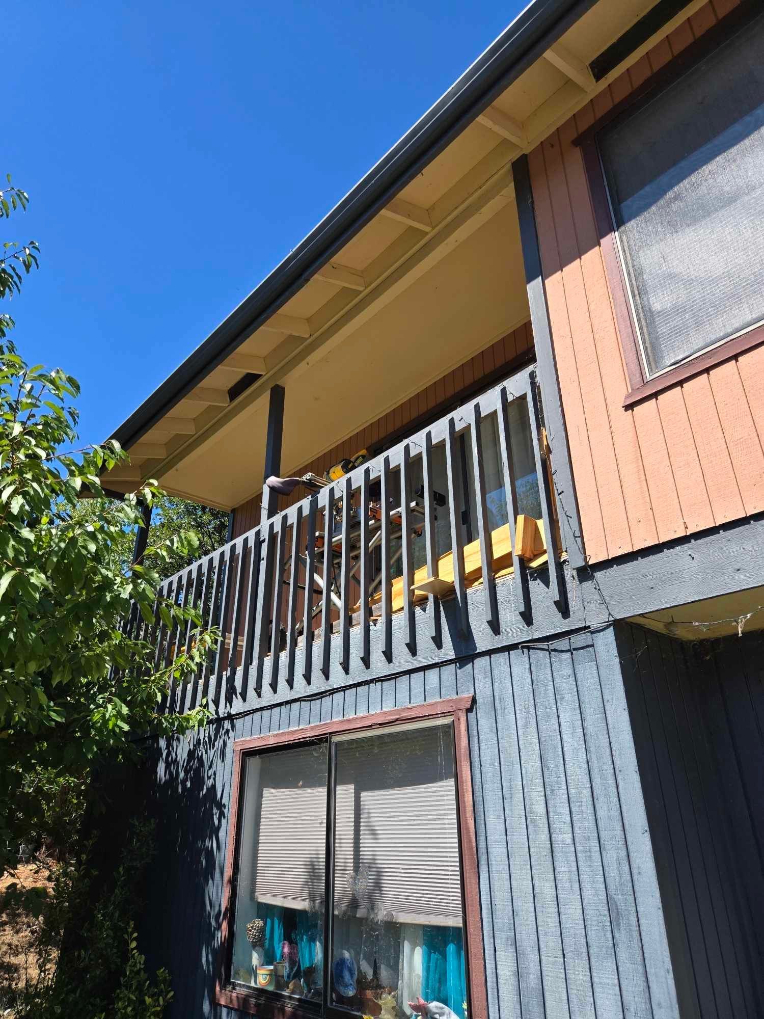Two-story house with a balcony, blue siding, and orange upper exterior under a clear sky