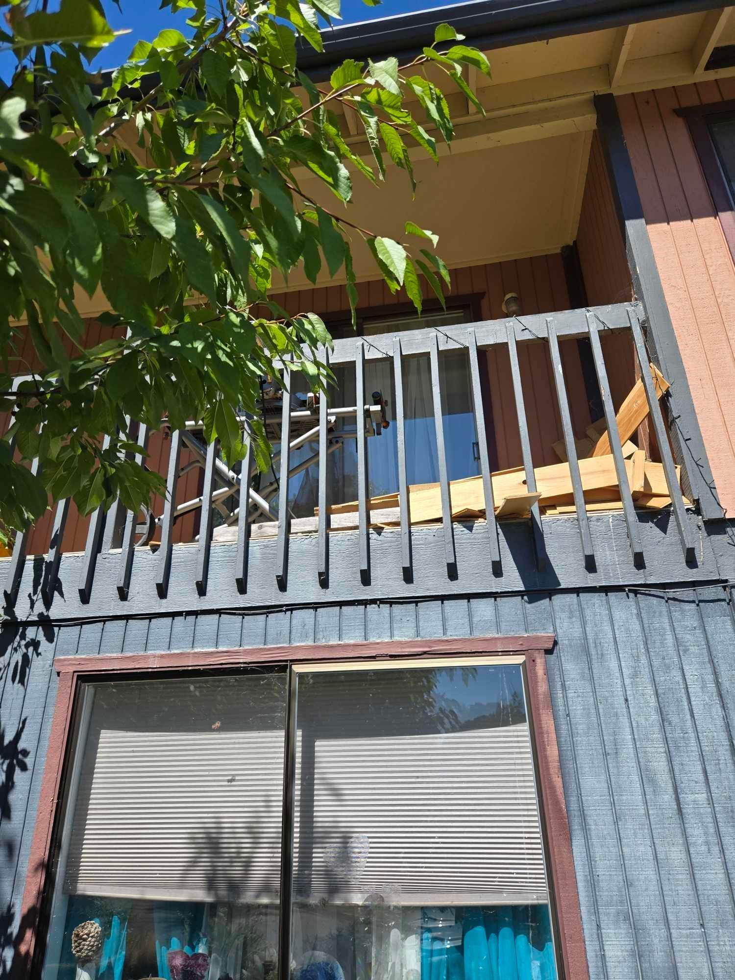Balcony with white railings above a window, partially shaded by tree leaves on a house exterior.