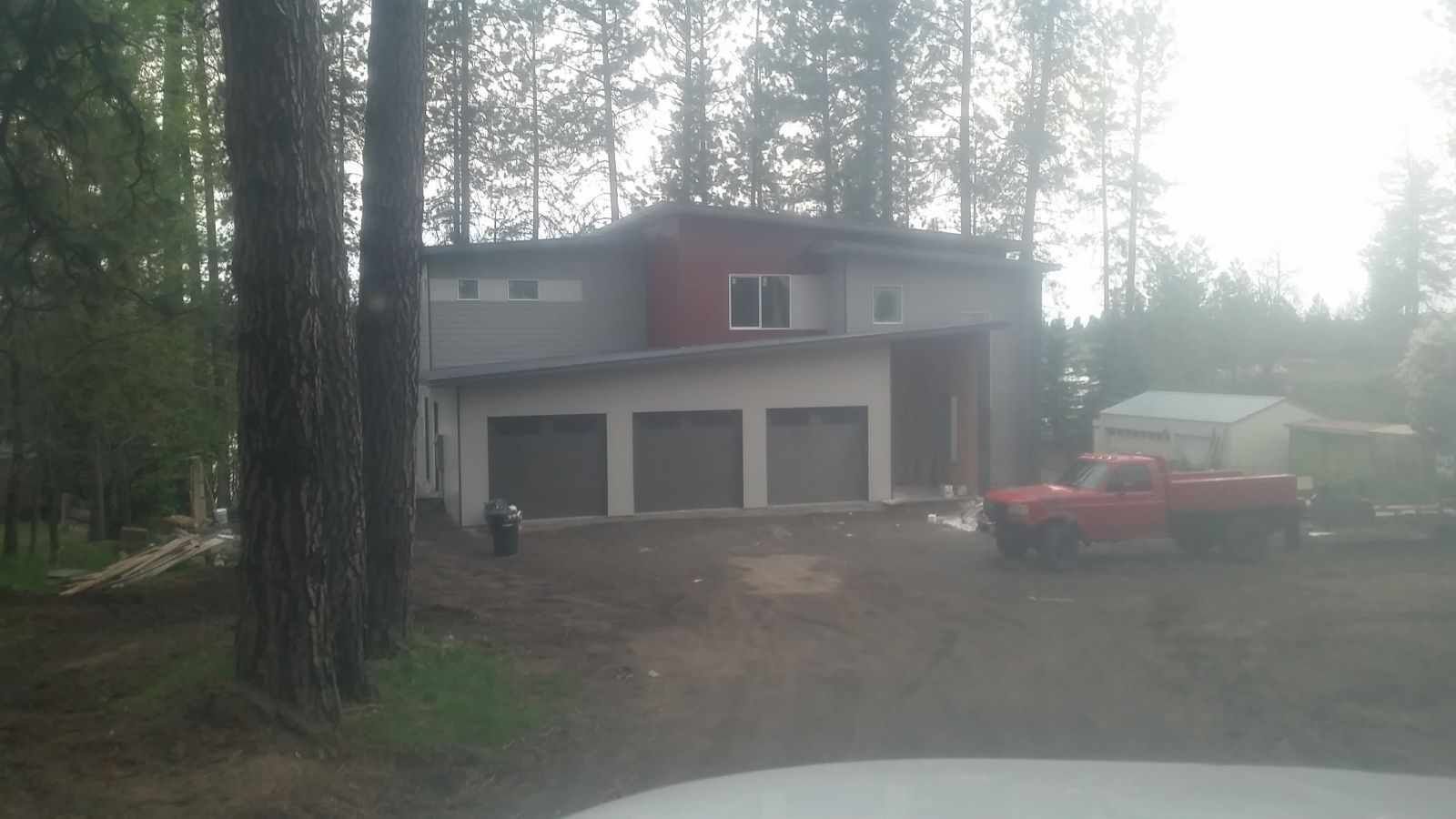 Two-story house in a wooded area with a three-car garage, red pickup truck, and forest clearing.