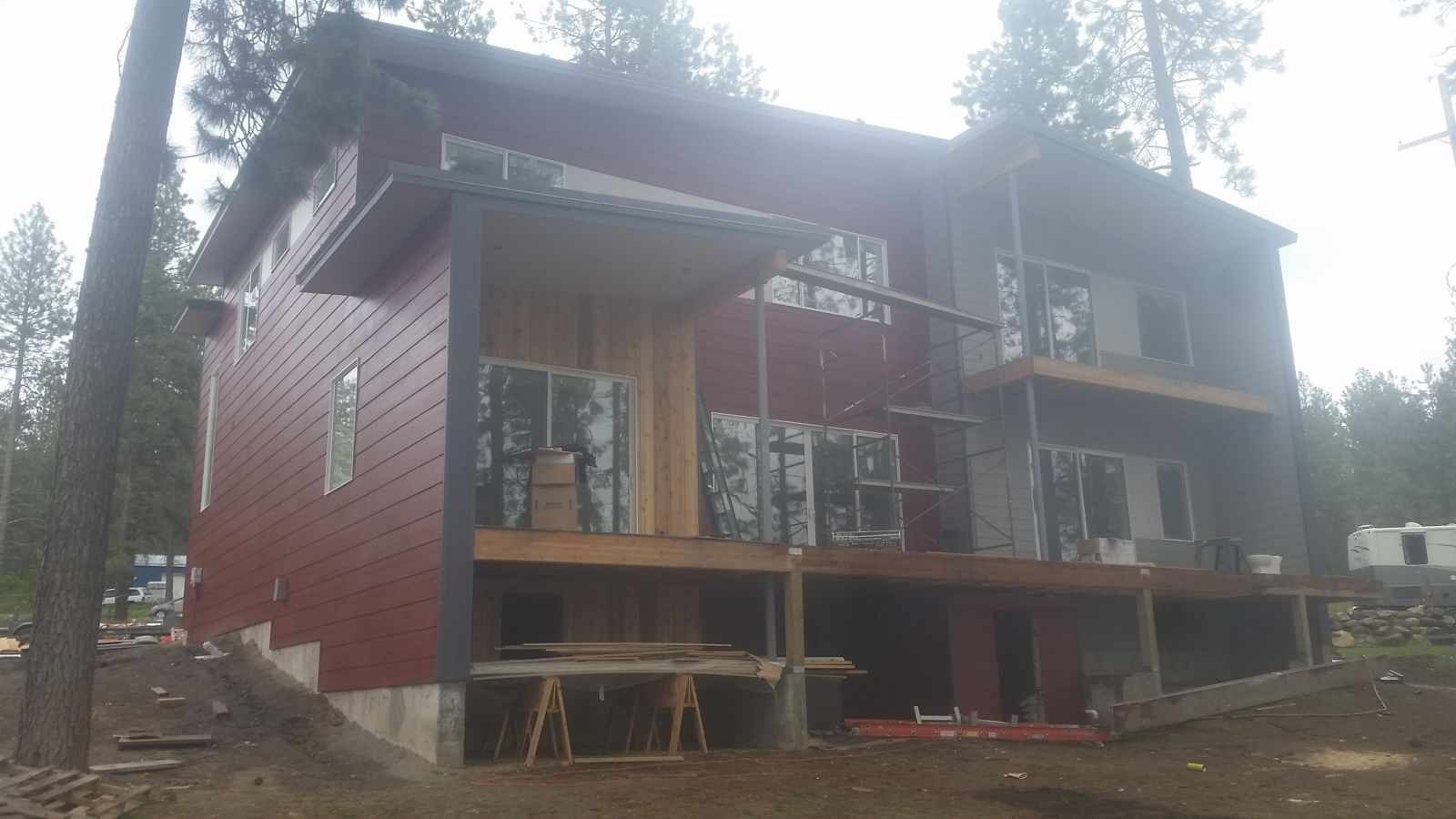 Two-story red house under construction with a covered porch and surrounding trees