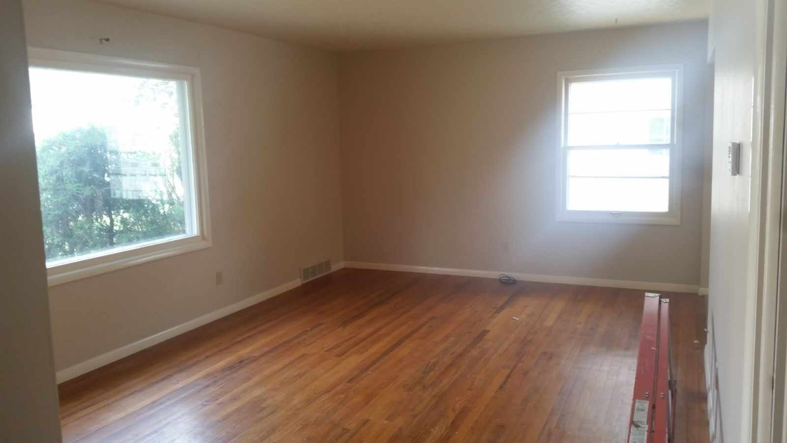Empty room with hardwood floors, beige walls, and two windows letting in daylight.