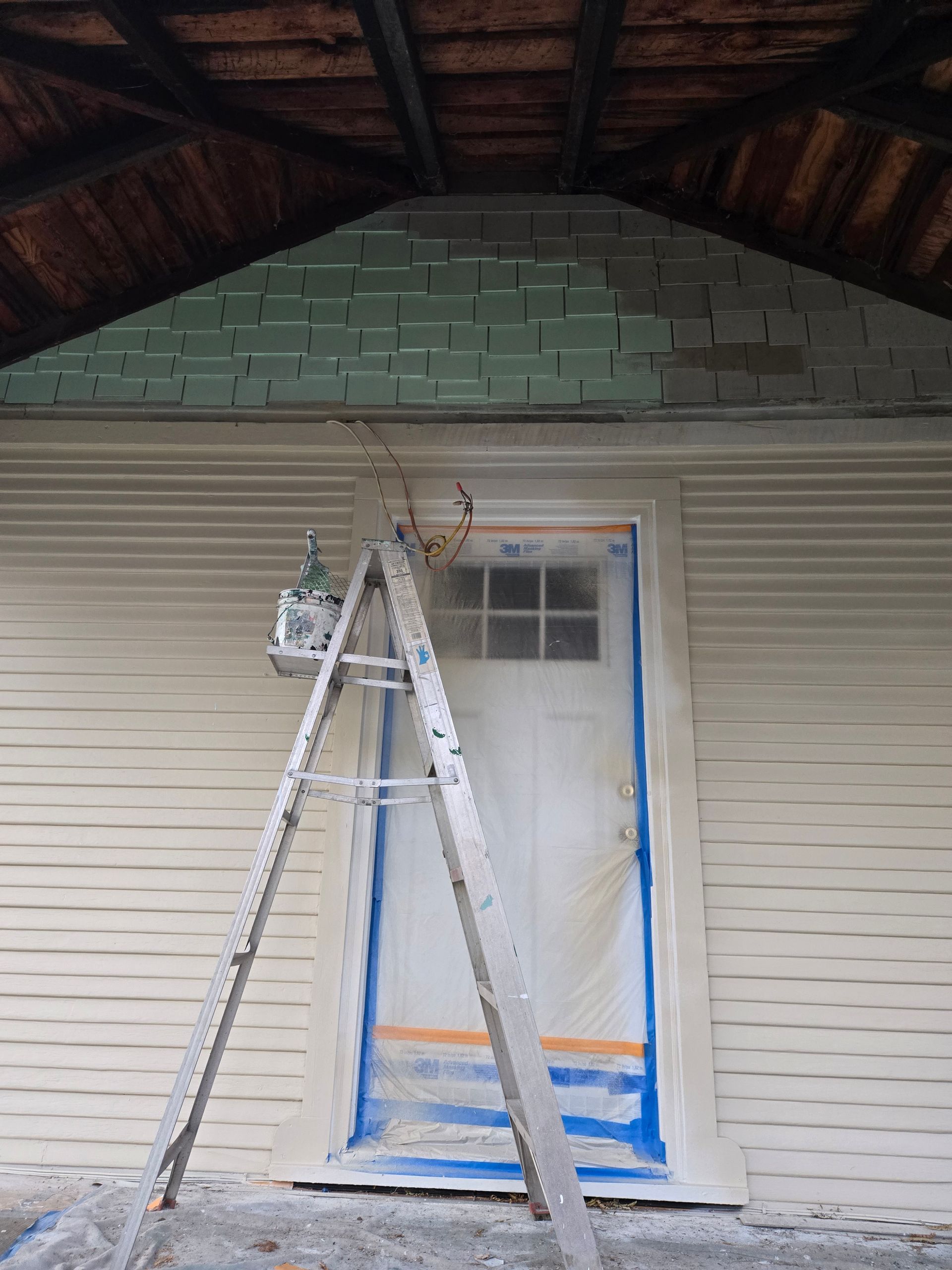 Ladder on a porch in front of a white door and siding, with blue painter’s tape around the doorway.