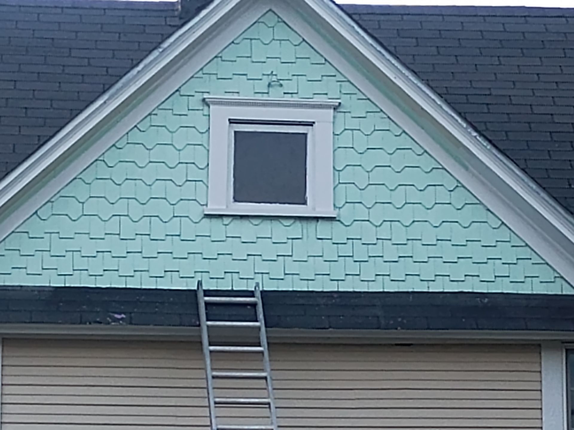 House gable with mint-green shingles, small dormer window, and a ladder leaning against the roof.