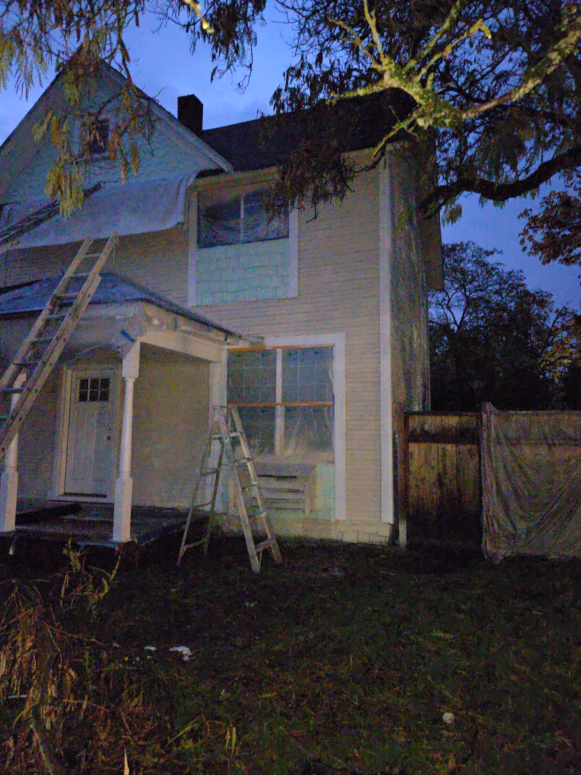 Two-story house at dusk with ladders and scaffolding under repair
