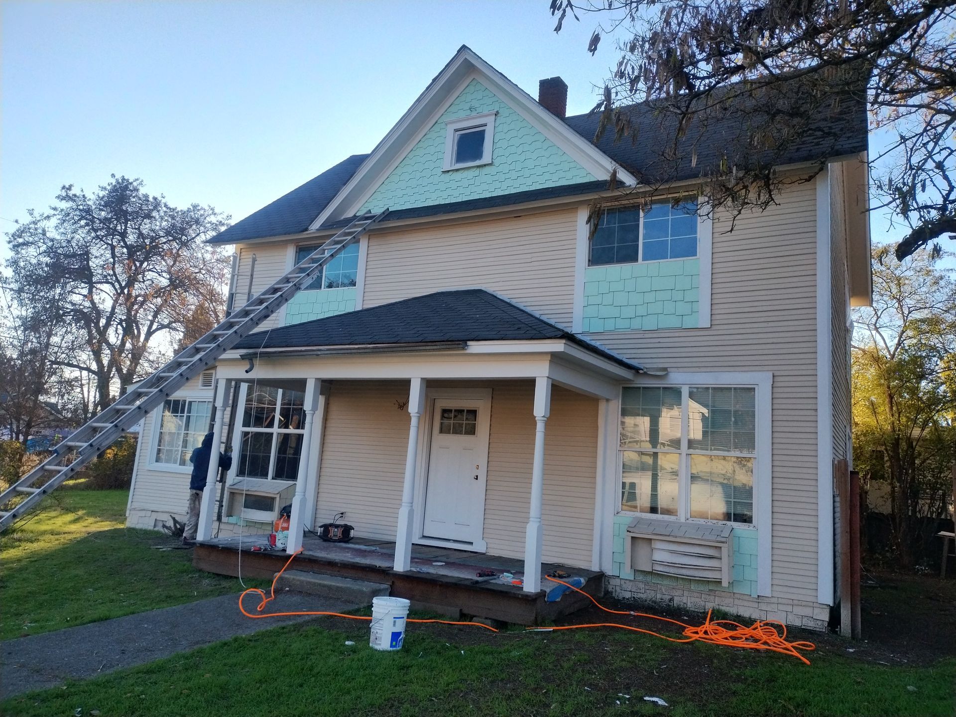 Two-story beige house with porch, blue roof trim, and orange extension cords on the lawn