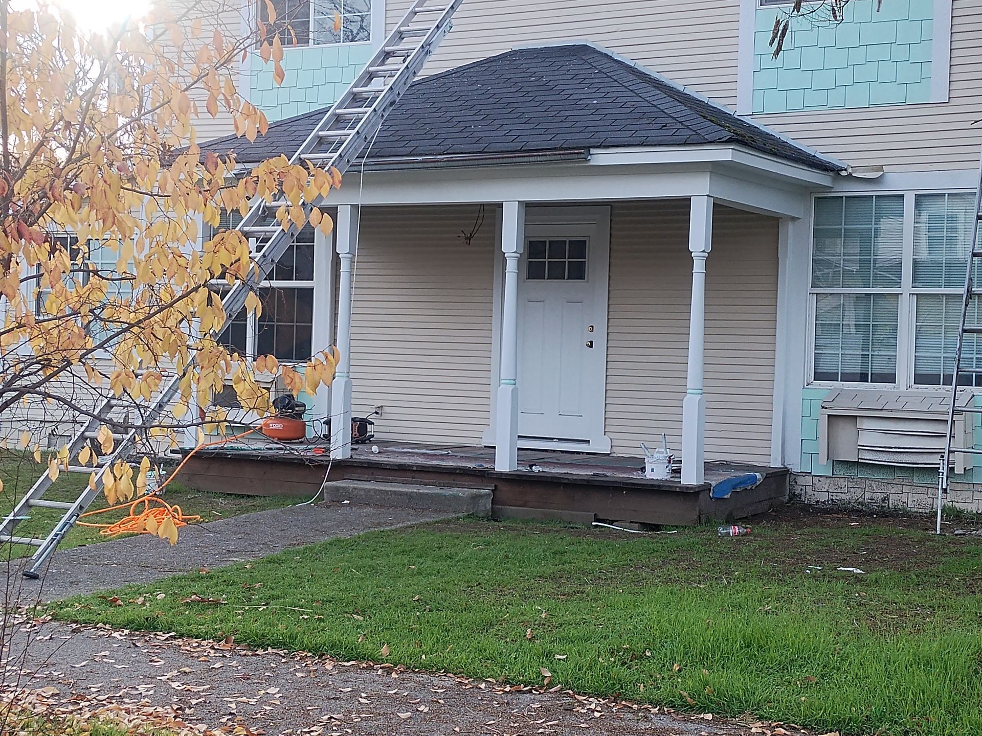 Small house entrance with white porch, broken window, and autumn tree in front yard.