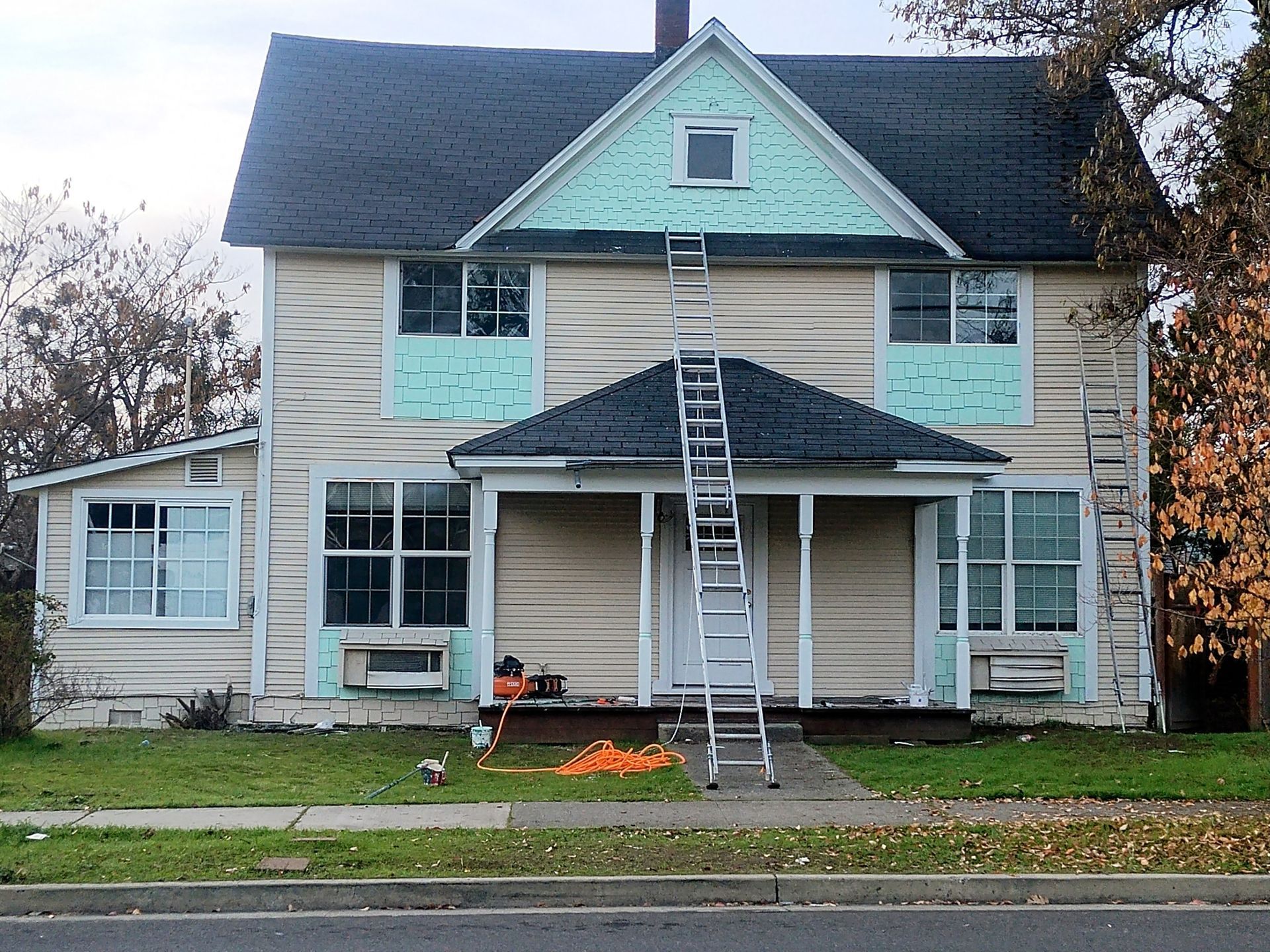 House exterior with ladders and fresh paint, showing ongoing renovation work on the front porch and upper facade
