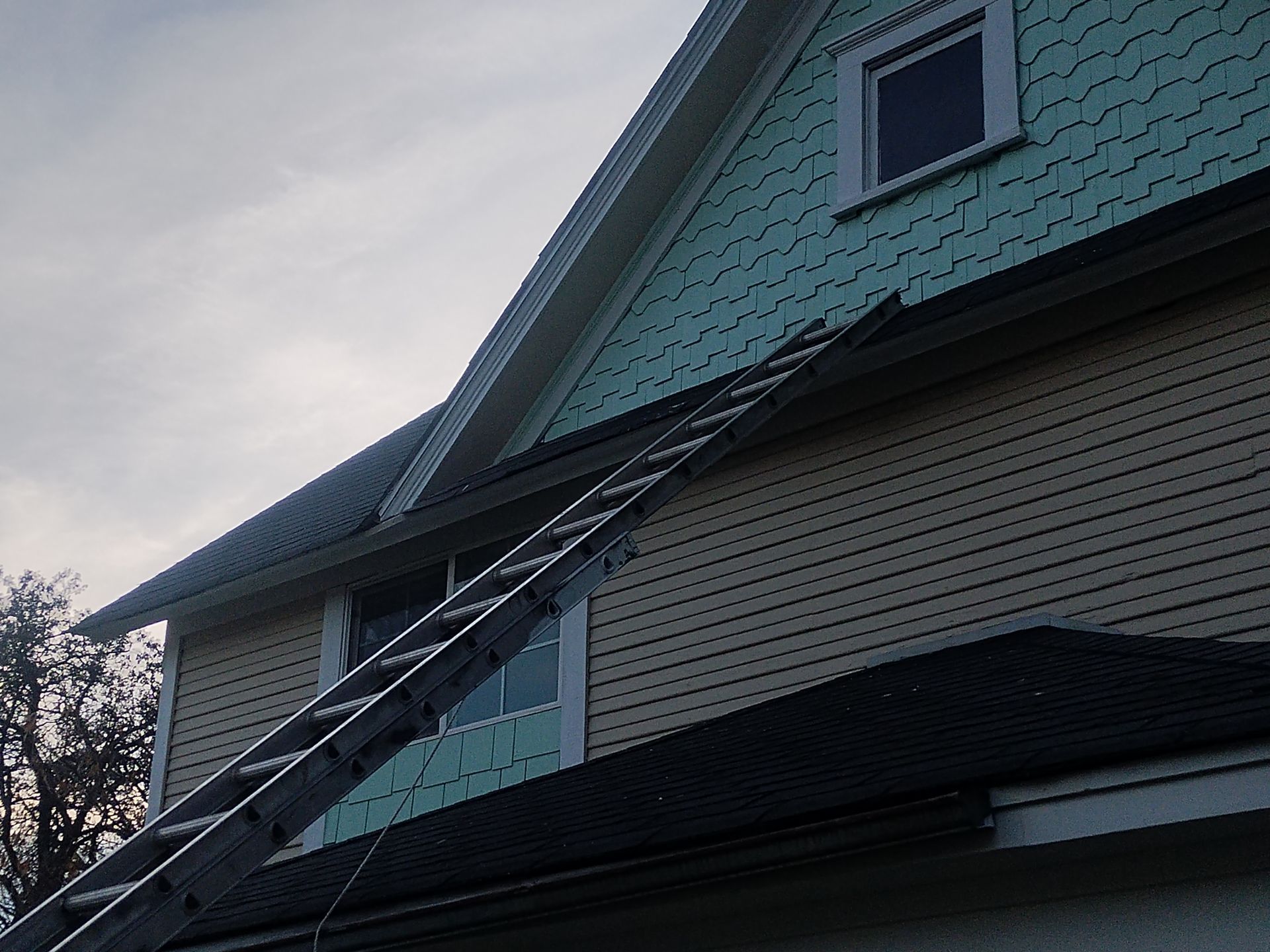 Ladder leaning against a house roof beneath a dormer window at dusk