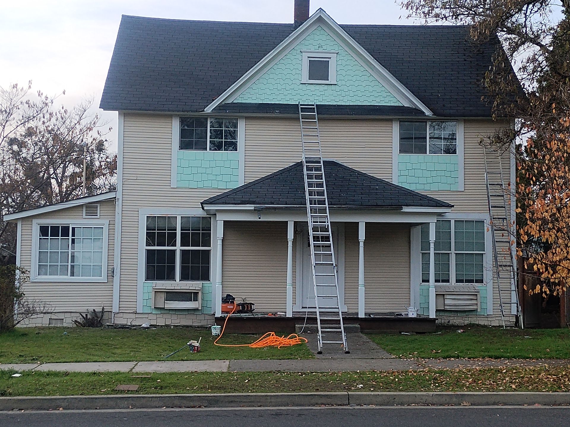 Two-story house with ladders and scaffolding at the front, roof and siding being repaired