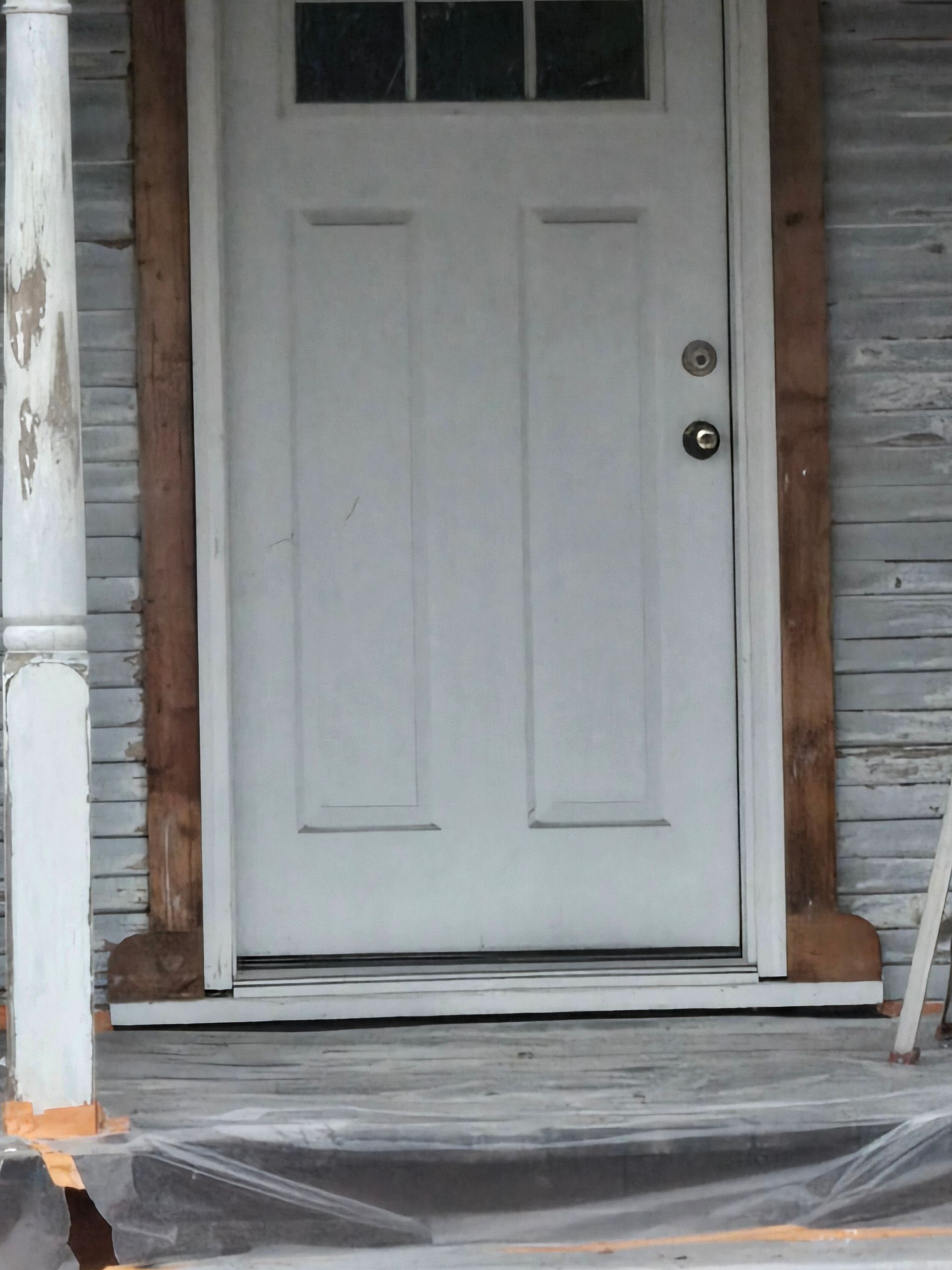 White front door with steps and plastic-covered porch in front of a weathered house