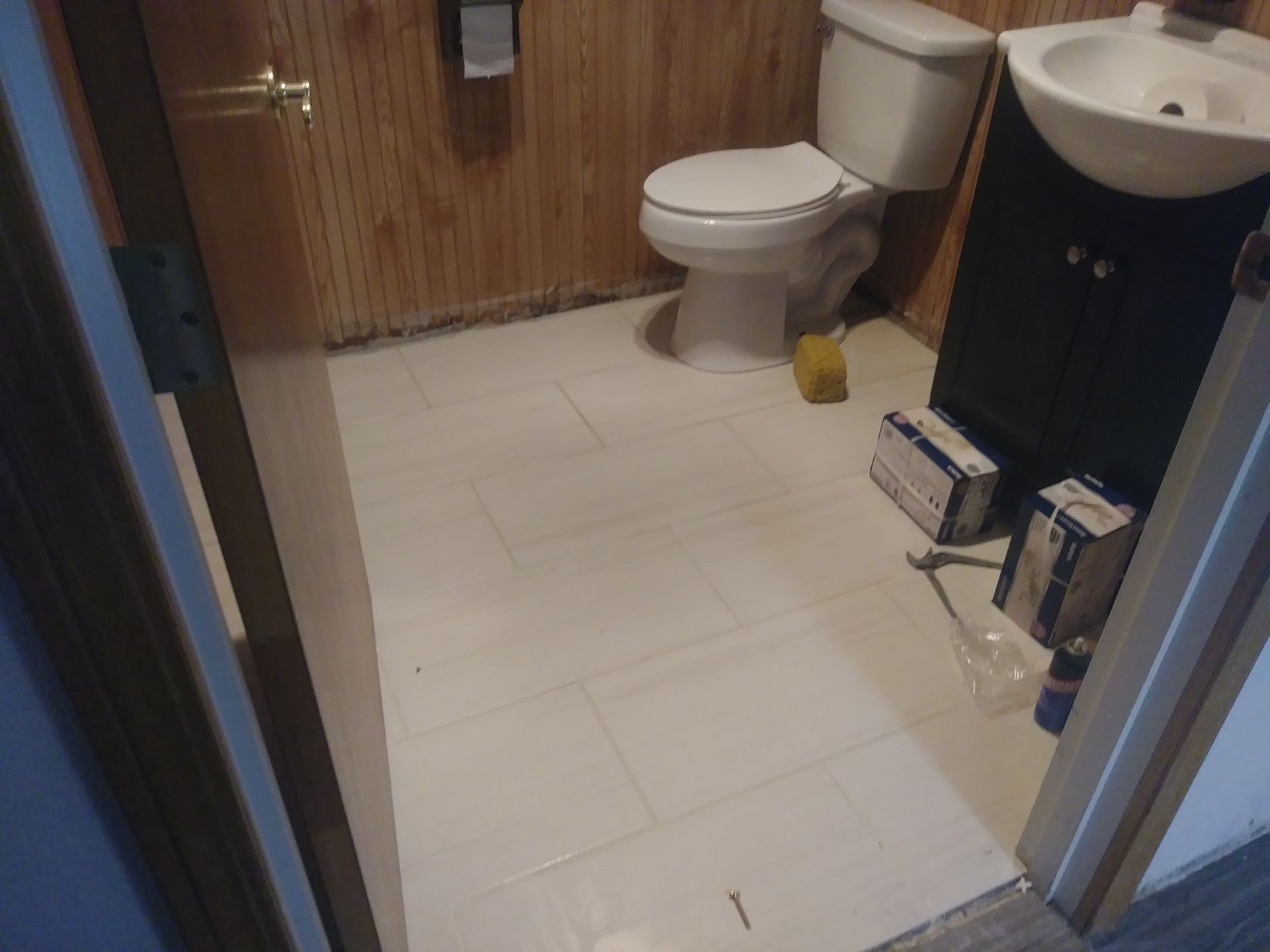 Small bathroom with toilet, sink, and tiled floor; blue towel rack and cleaning items near the door.