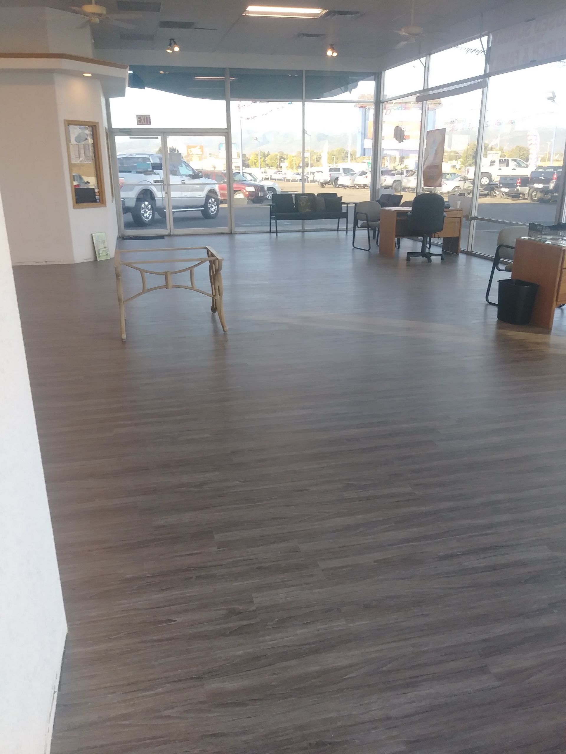 Spacious storefront interior with wood floor, chairs, tables, and large windows overlooking a parking lot.
