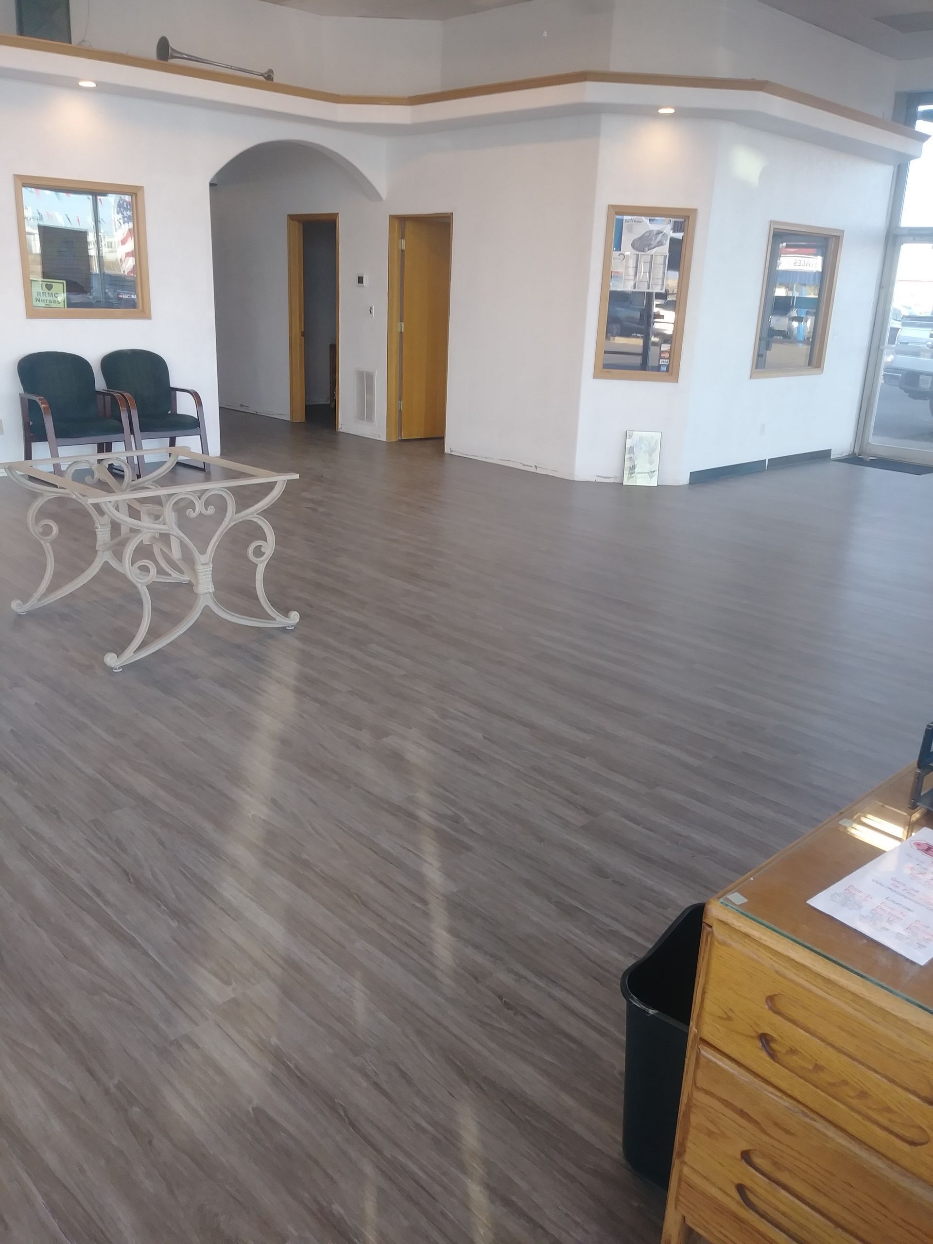 Empty waiting room with gray wood floors, arched doorway, chairs, and a wooden desk in the corner