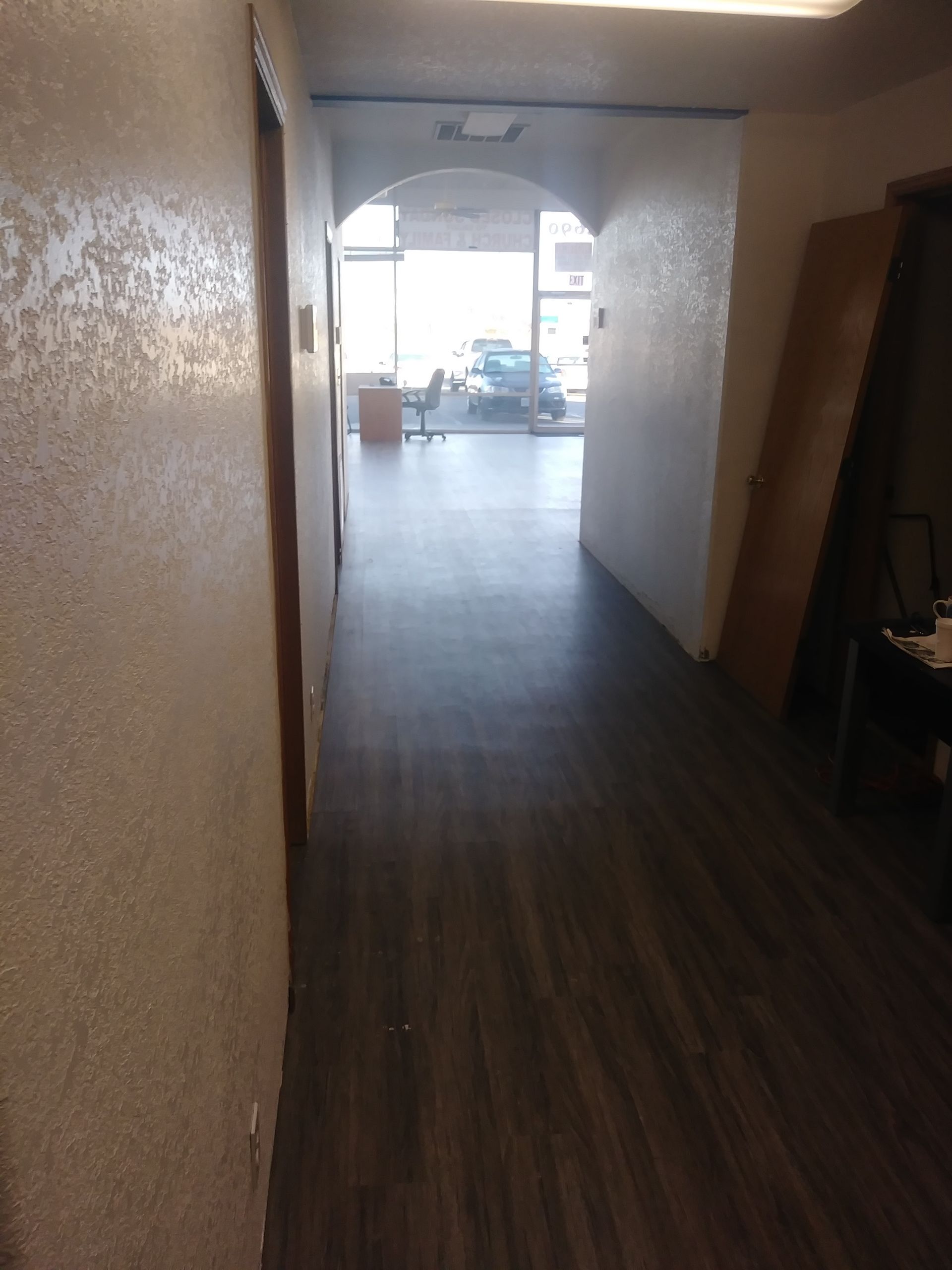 Empty indoor hallway leading to a bright arched entrance and street view beyond