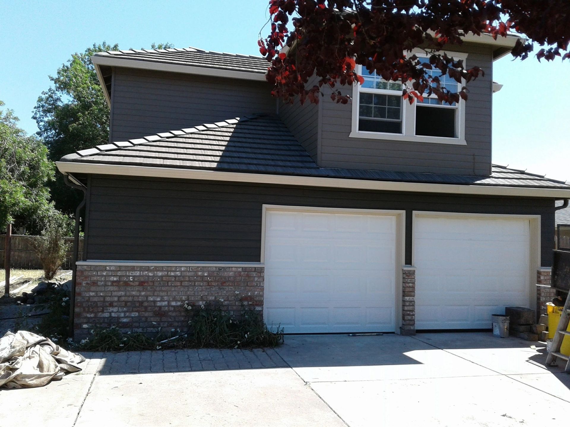 Two-story gray house with white garage doors, brick lower facade, and a driveway in front.