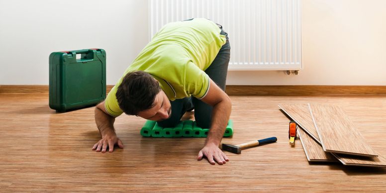 Person repairing a floor, kneeling on boards with tools and a green toolbox nearby