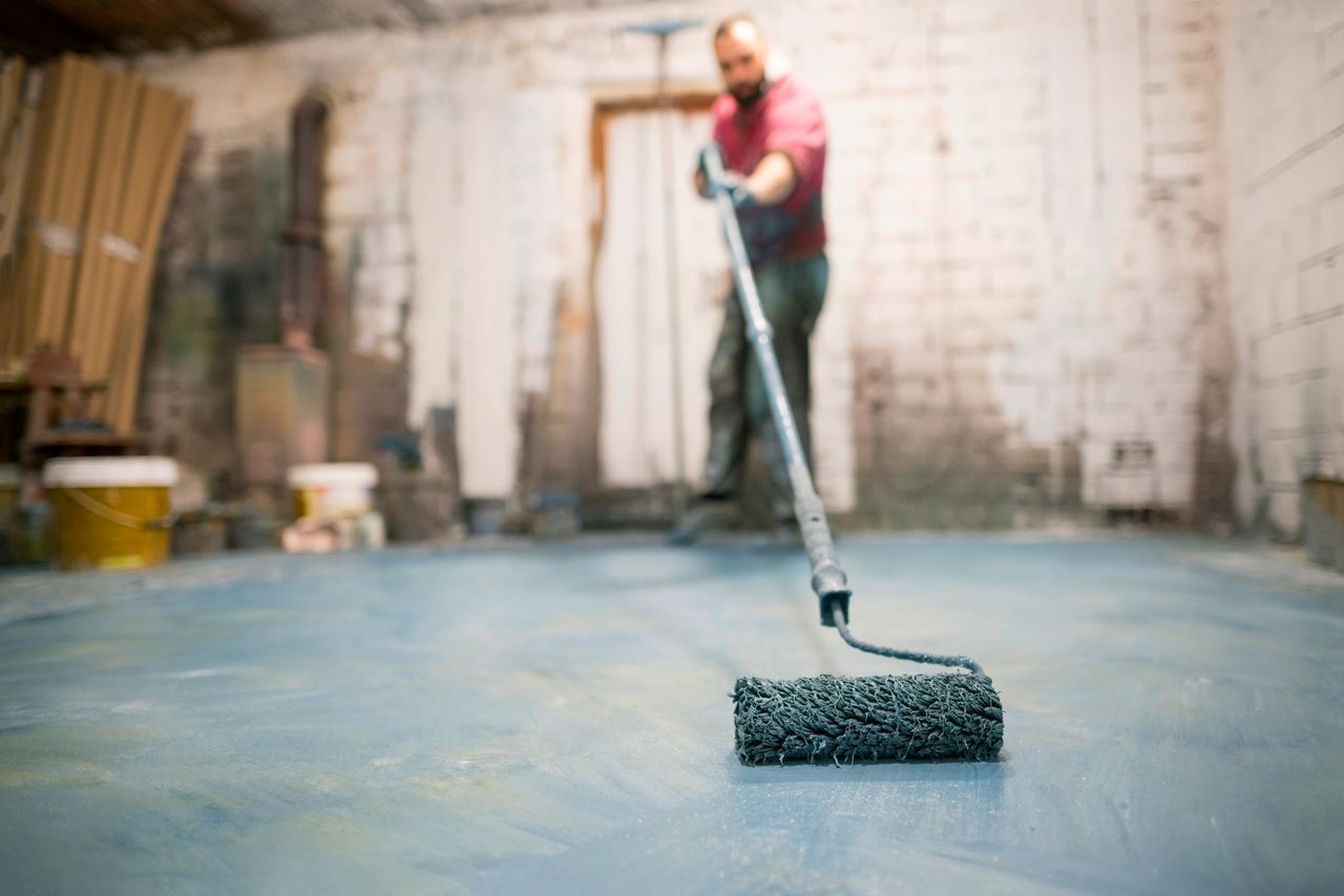 Worker painting a floor in a workshop with a roller and blue coating