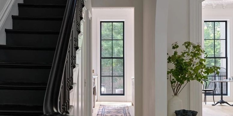 Bright entryway with black staircase, white walls, and a potted tree by a sunlit window.
